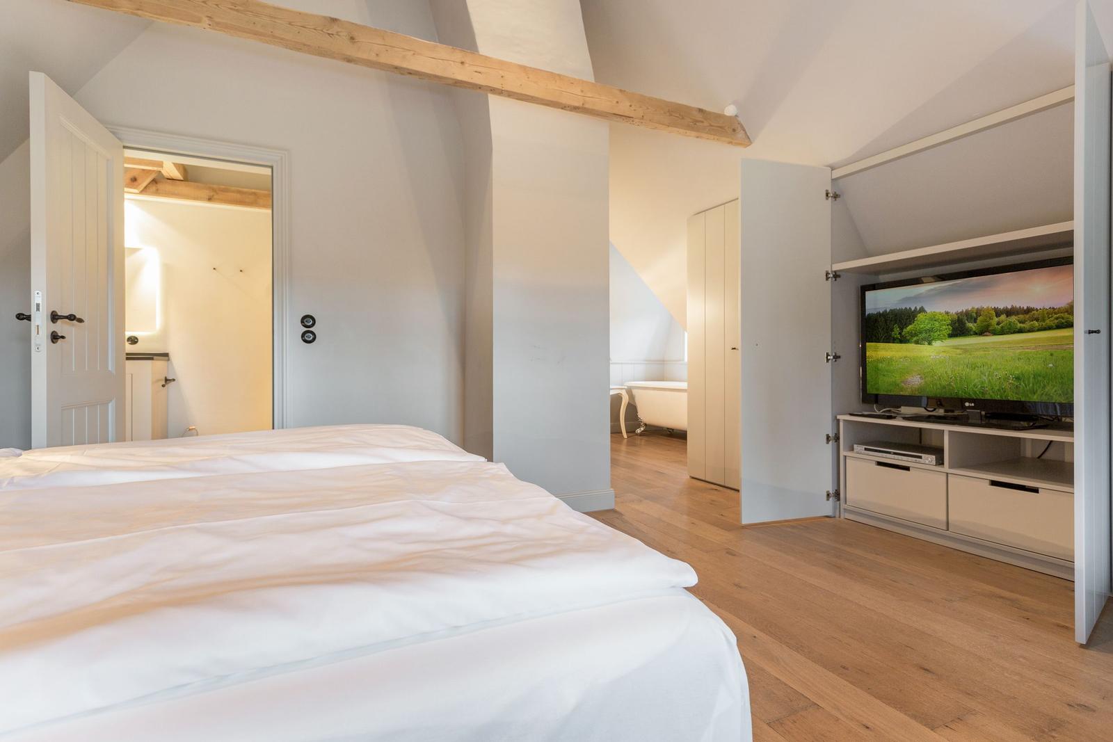 Schlafzimmer mit Doppelbett, TV und angrenzender Badewanne.