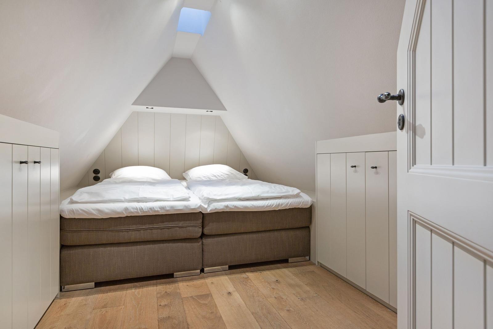 Schlafzimmer mit Doppelbett, Holzboden und Dachschrägen. Weiße Schränke und Dachfenster.