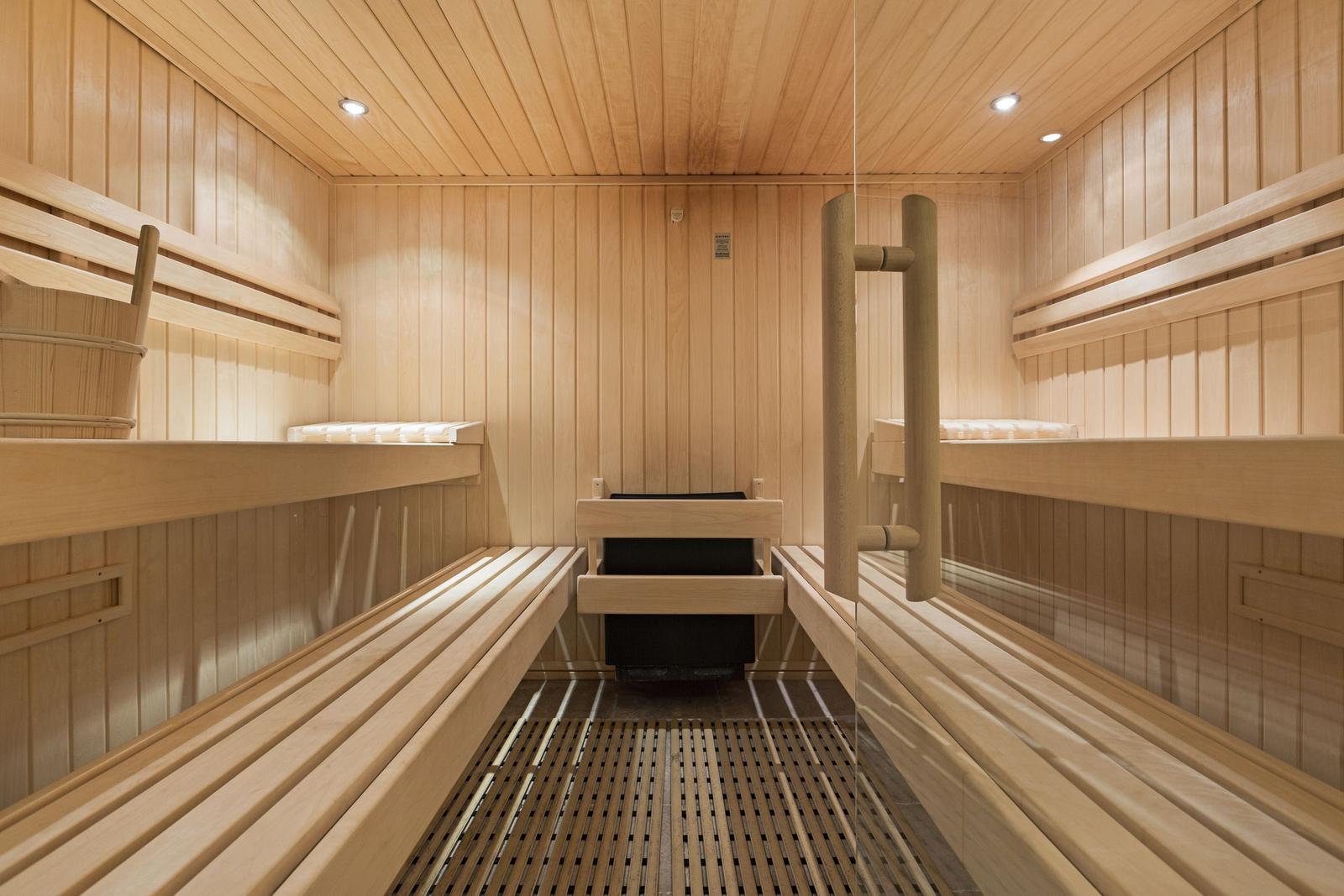 Holzsauna mit mehreren Sitzbänken und Heizung im Zentrum.