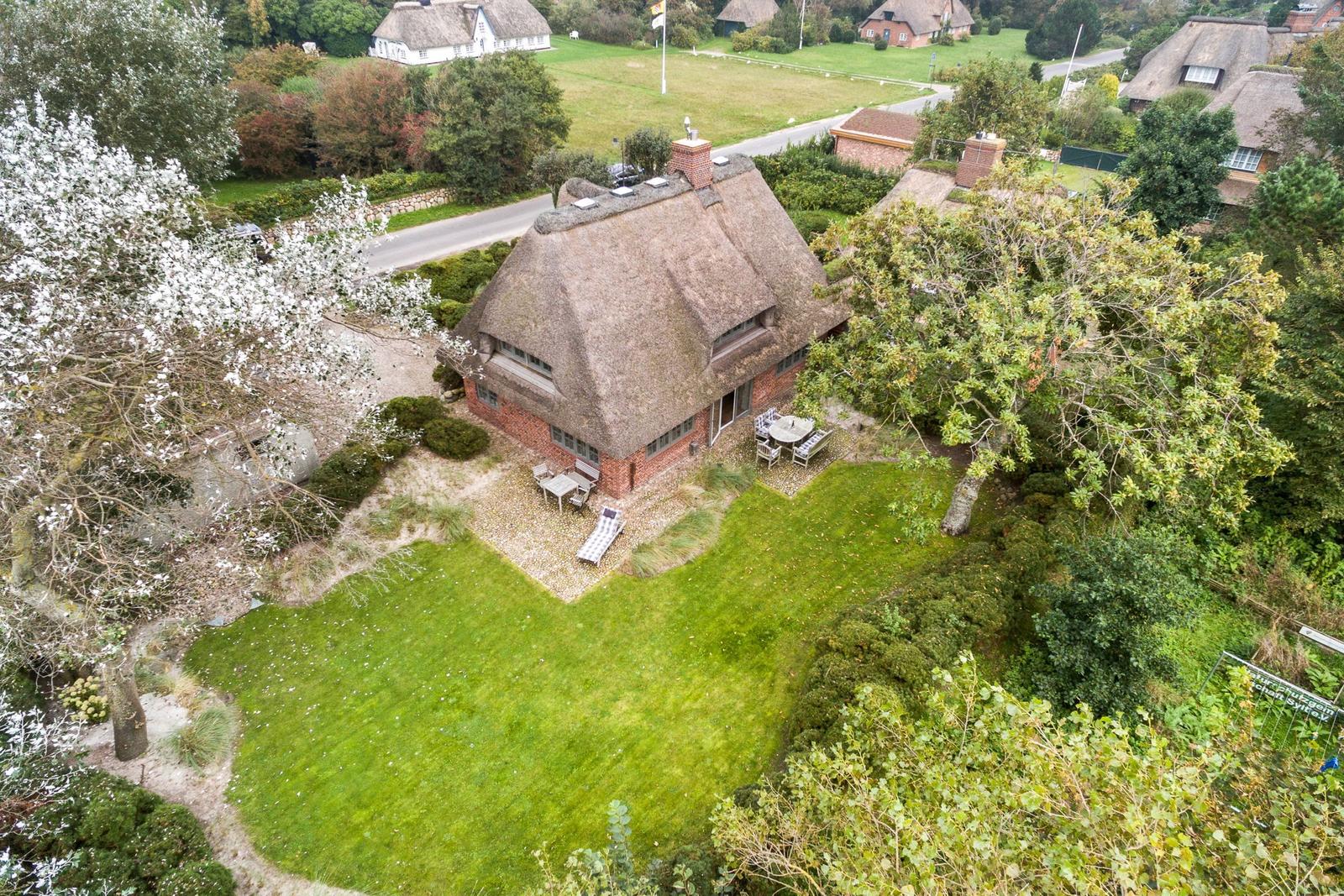 Haus mit Strohdach, Garten und Terrasse. Umgeben von Bäumen und Grünflächen.