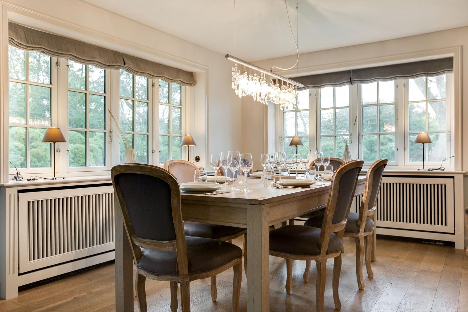 Esszimmer mit Holztisch, Stühlen und großen Fenstern.