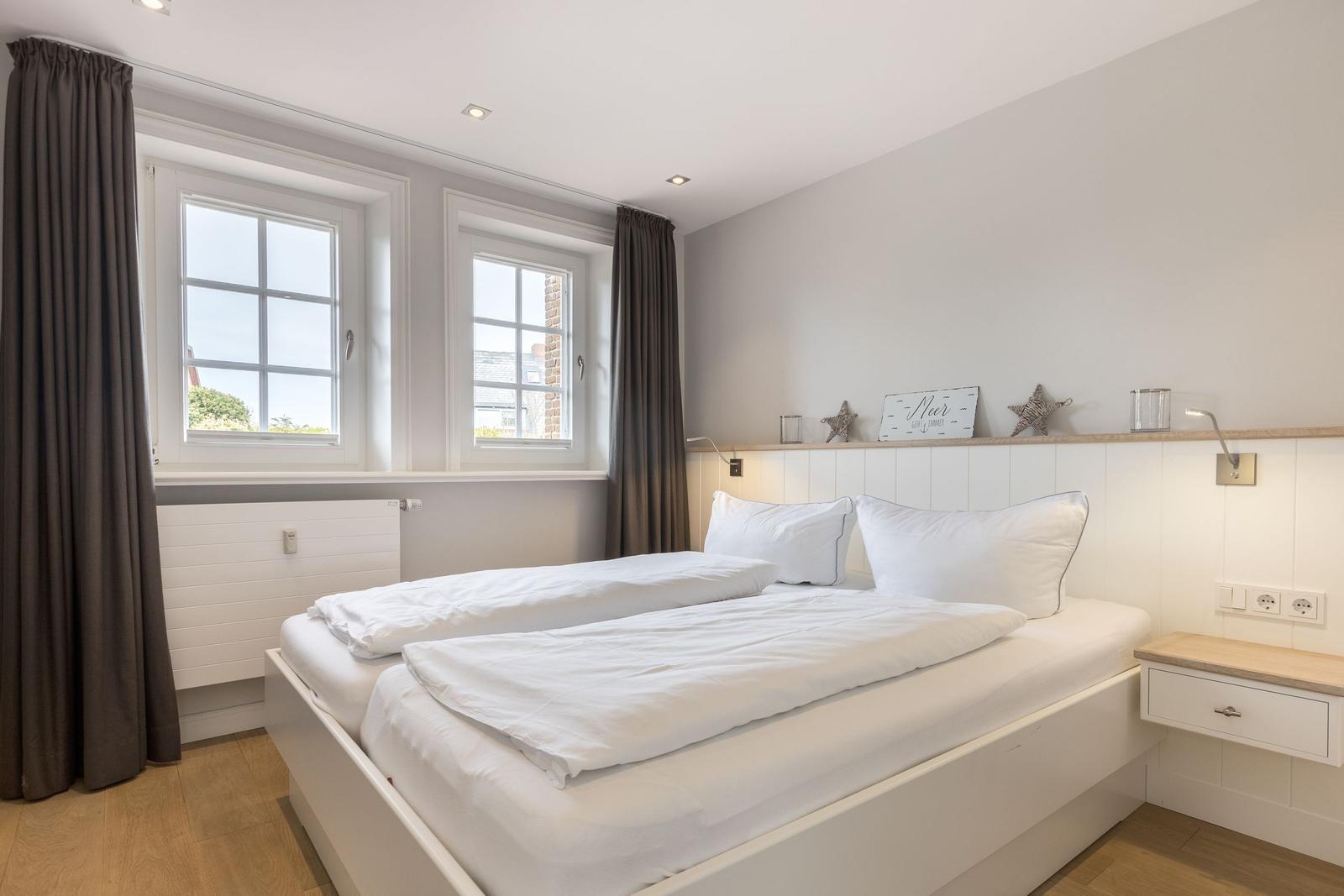 Bedroom with white bed, two windows, and wooden floor.