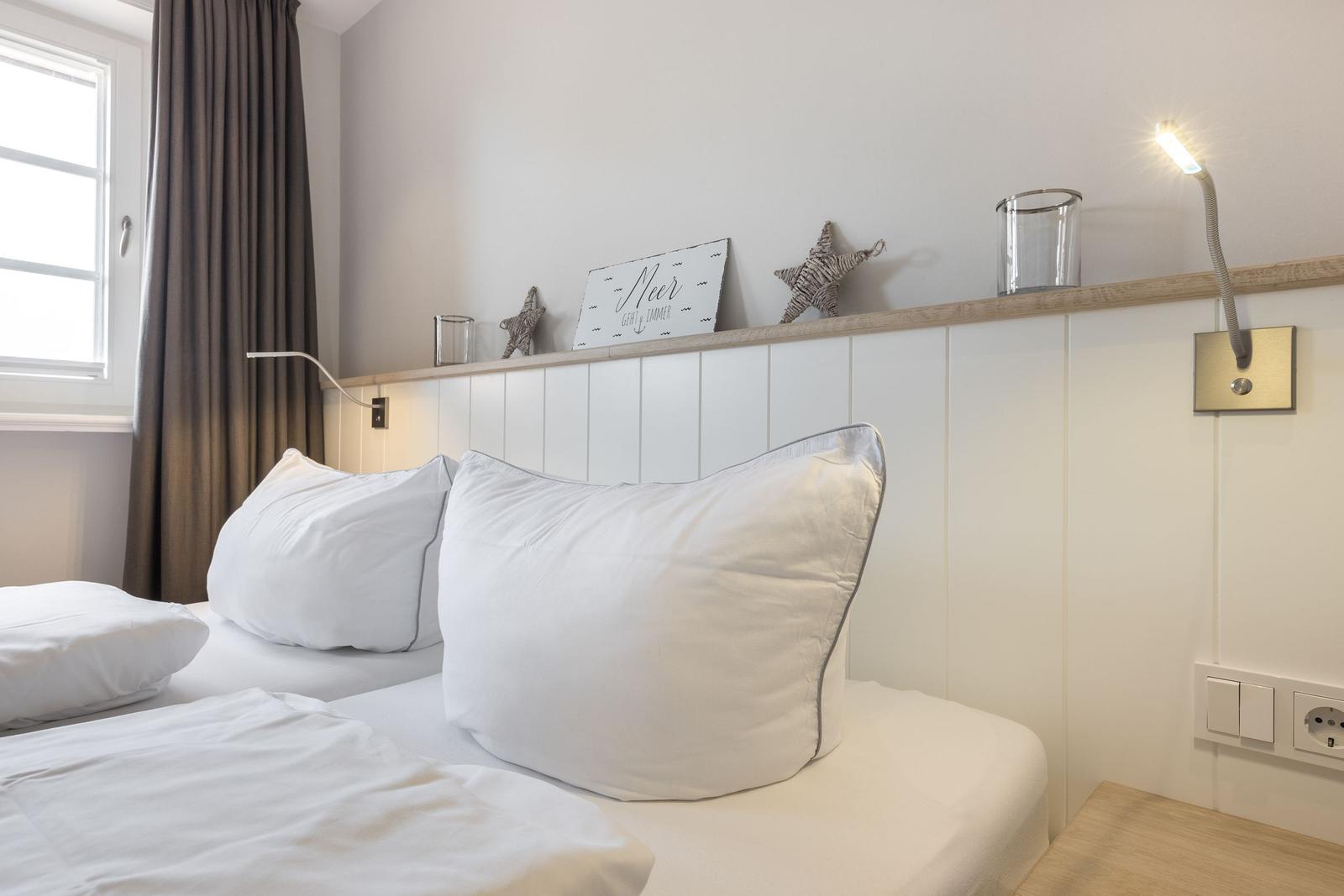 Bedroom with white bed, wood panels, and wall lighting.