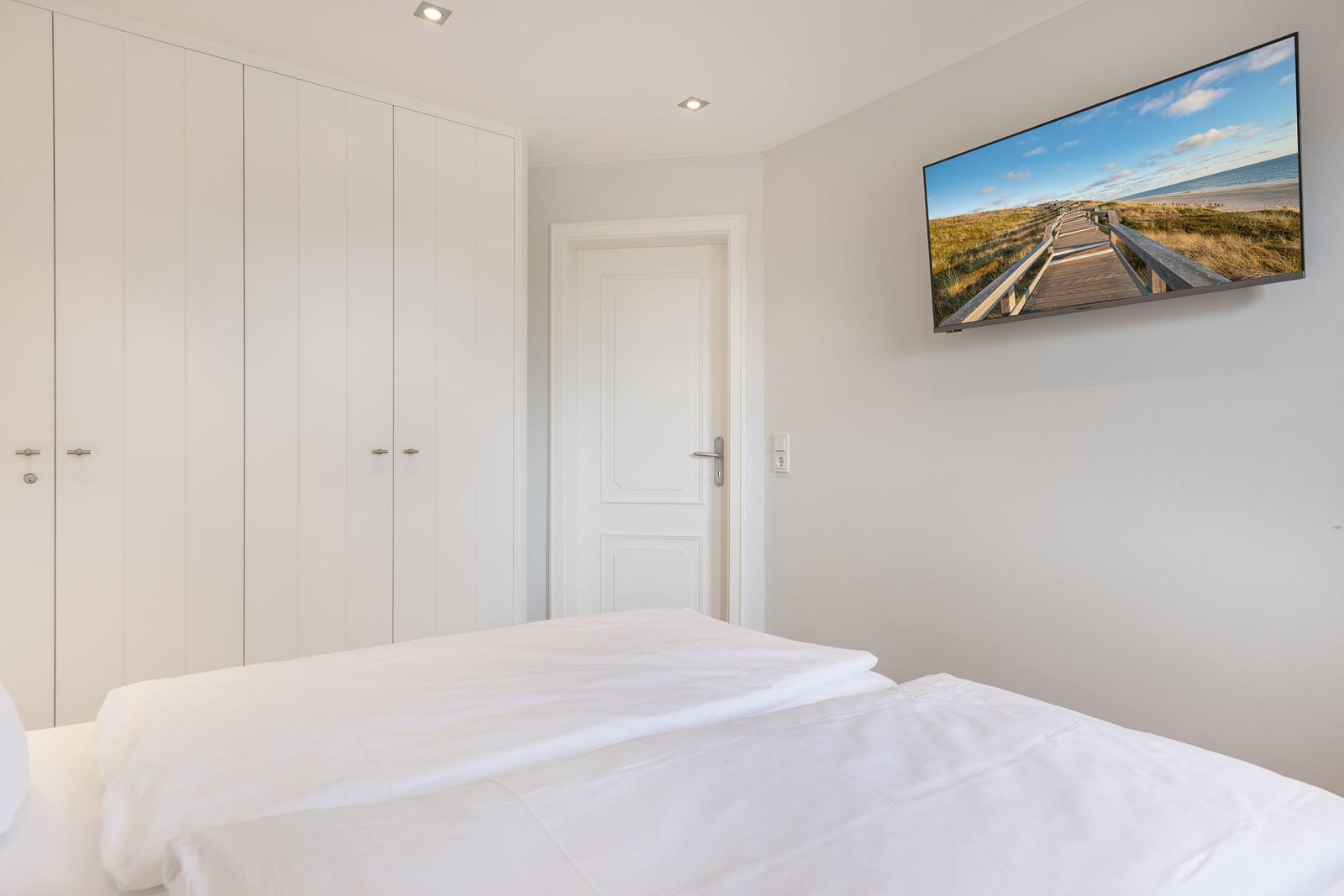 Bedroom with white bed, wardrobe, and wall picture of a beach.