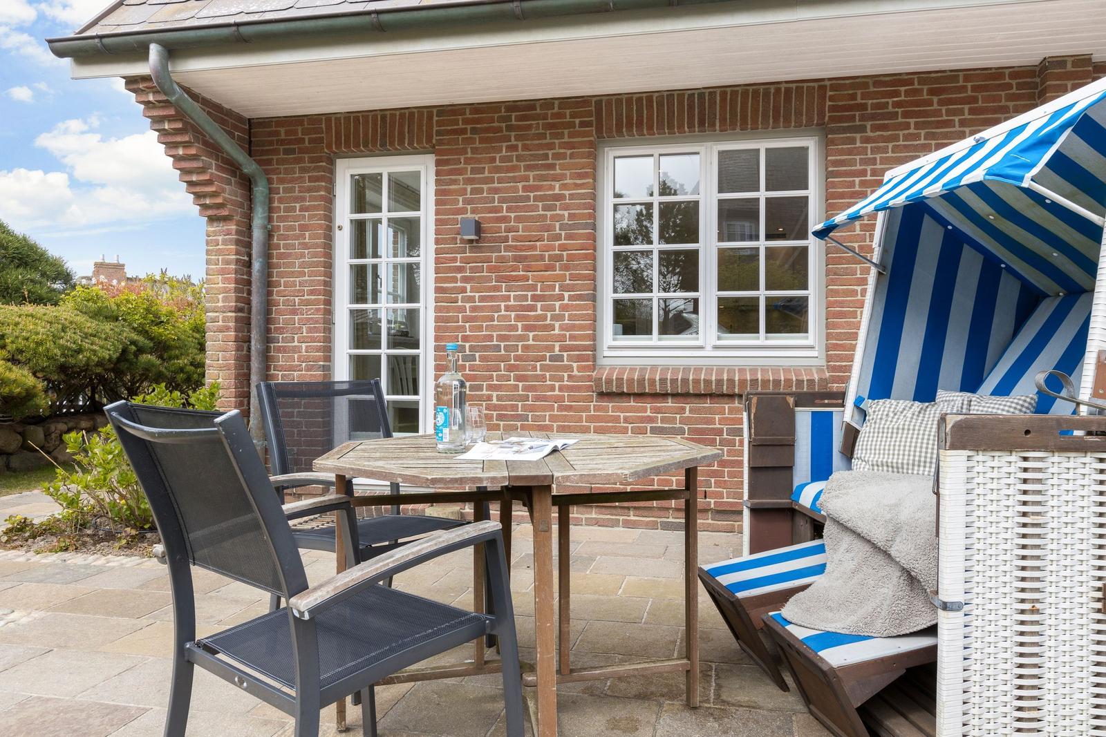 Terrace with table, chairs, and beach chair in front of brick house