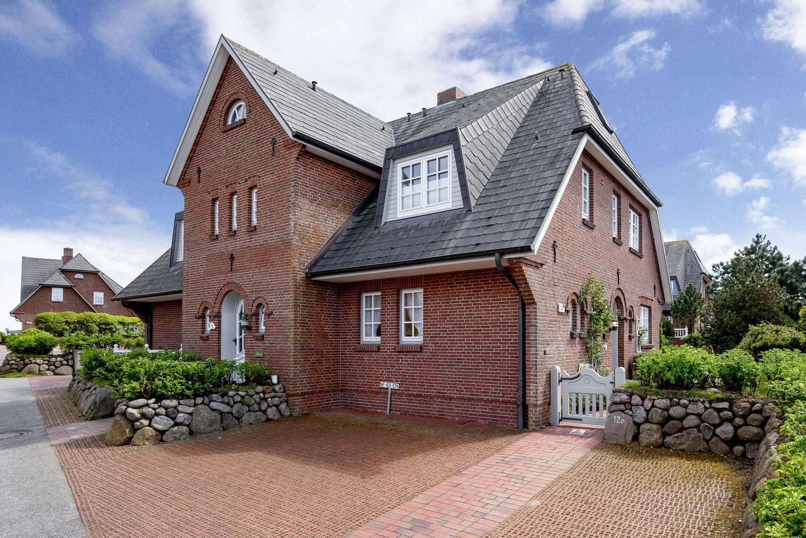 Red brick house with gray roof and paved yard.