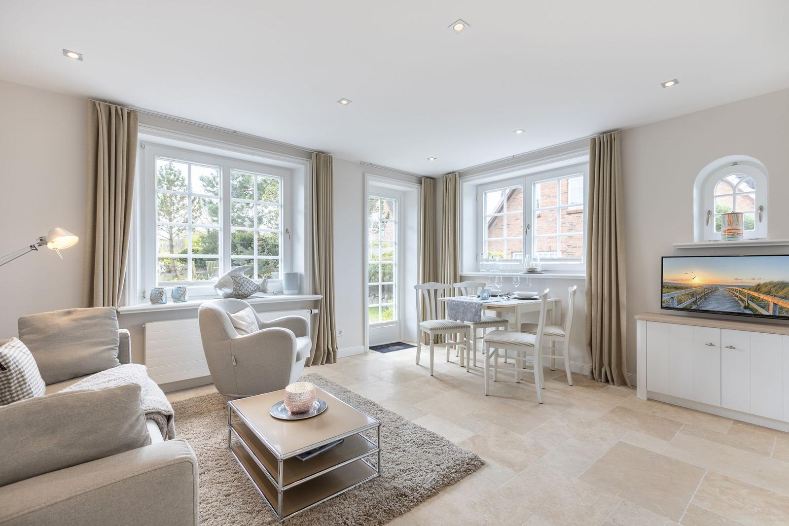 Living and dining area with windows, sofa, armchair, and TV.