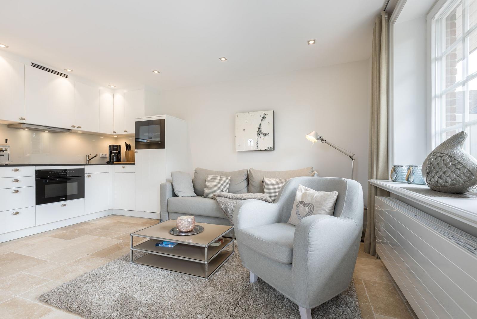Living and kitchen area with sofa, armchair, and kitchen appliances.