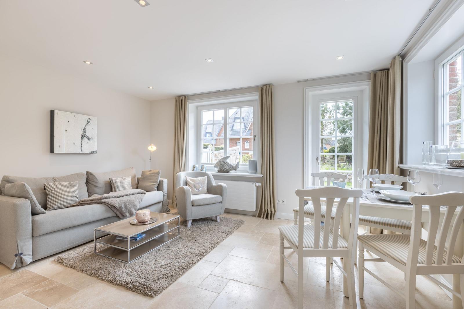 Living and dining area with sofa, armchair, table and chairs. Windows with curtains and view of garden.