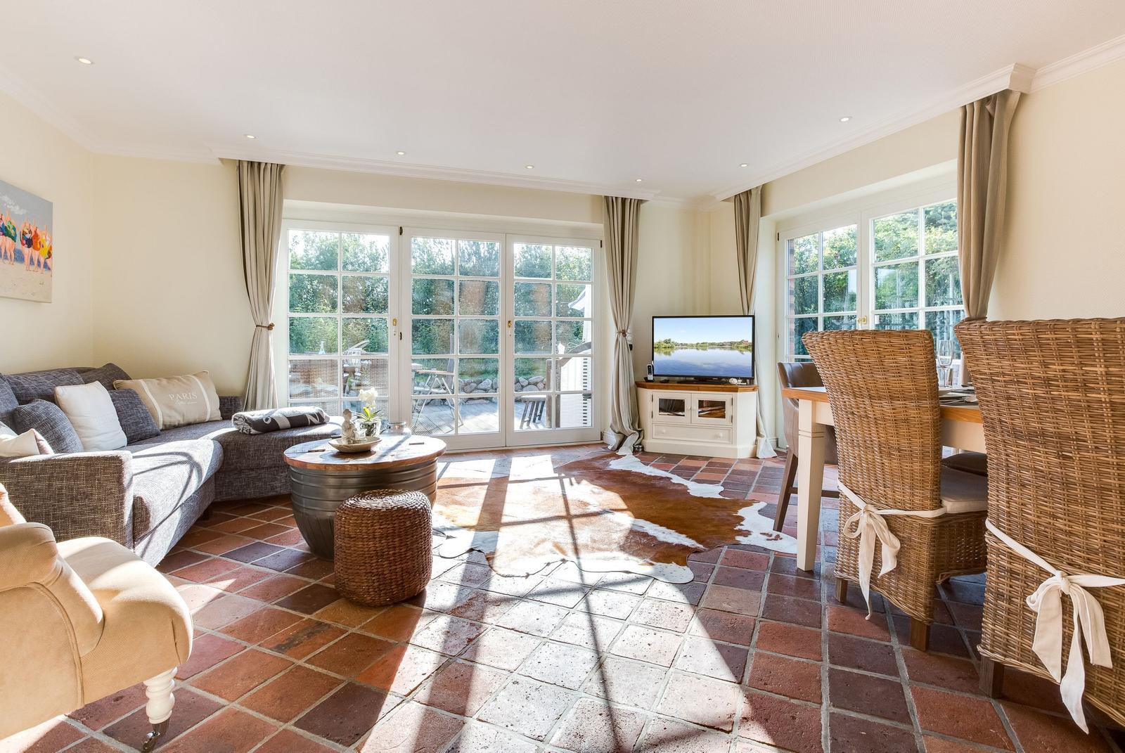 Wohn- und Essbereich mit Terrassentür, TV und Wickerstühlen auf Terrakottboden.