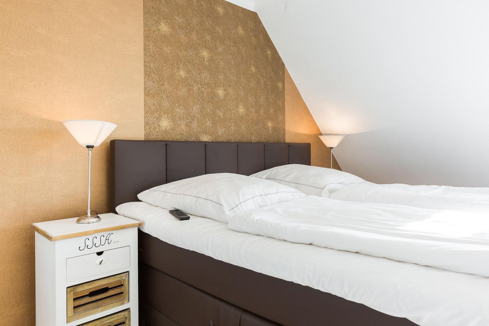 Schlafzimmer mit Bett, Nachttisch und Lampen an der Wand