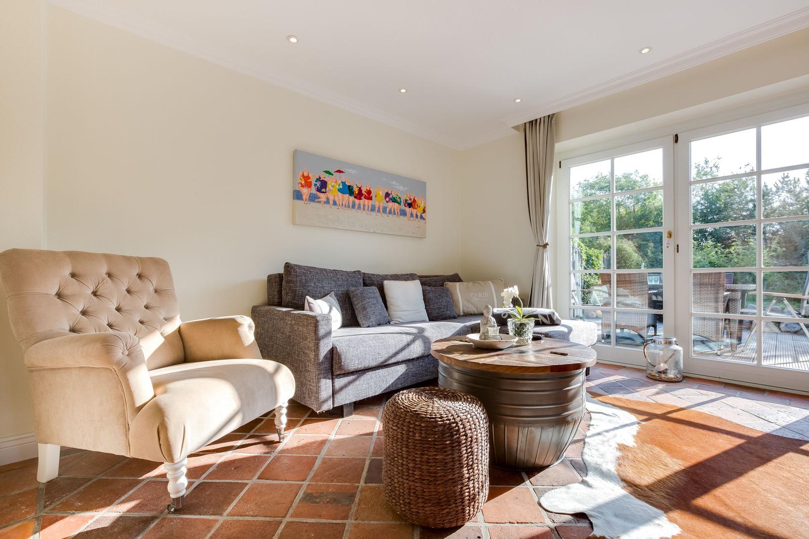 Wohnzimmer mit Sofa, Sessel, Tisch und Terrassentür.