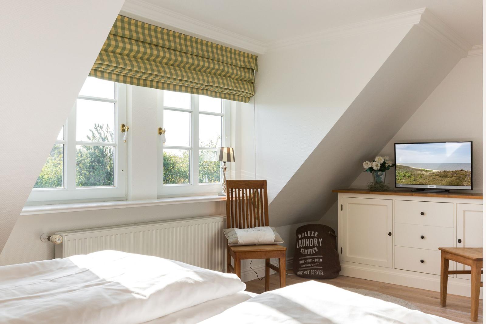Schlafzimmer mit Dachschräge, Fenster, Bett, Stuhl und TV-Schrank.