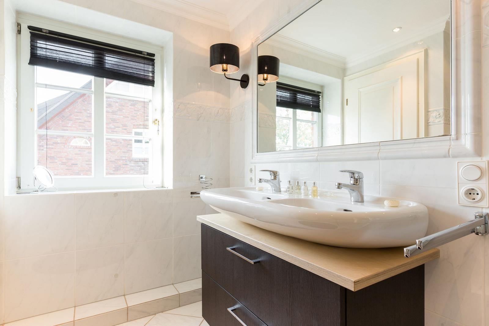 Badezimmer mit Waschbecken, Spiegel und Fenster.