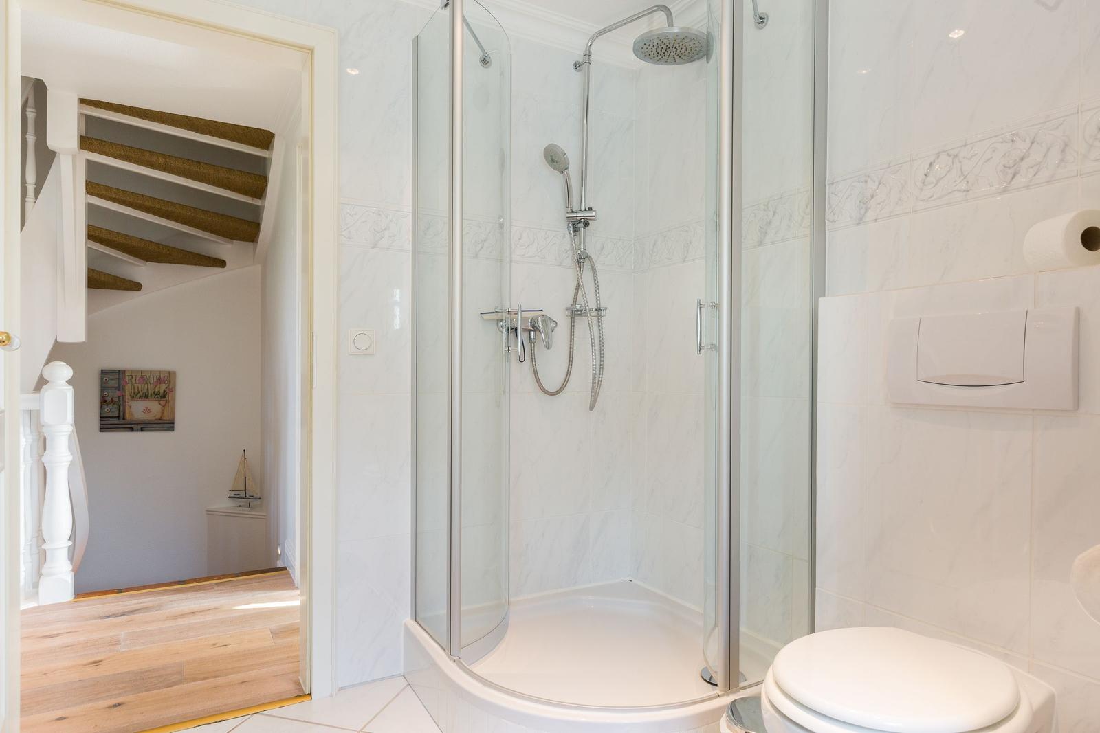 Dusche mit Glaswand, Toilette und Blick in Wohnbereich mit Treppe.