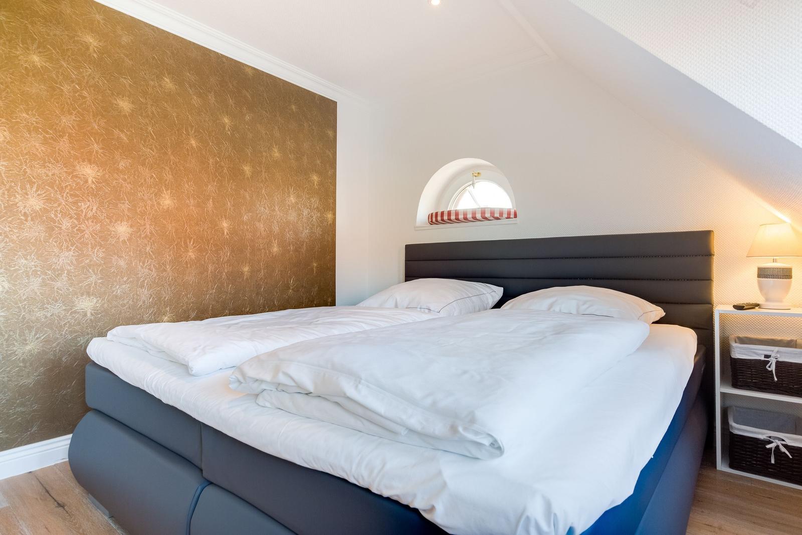 Schlafzimmer mit Doppelbett, goldener Wand und kleinem Fenster