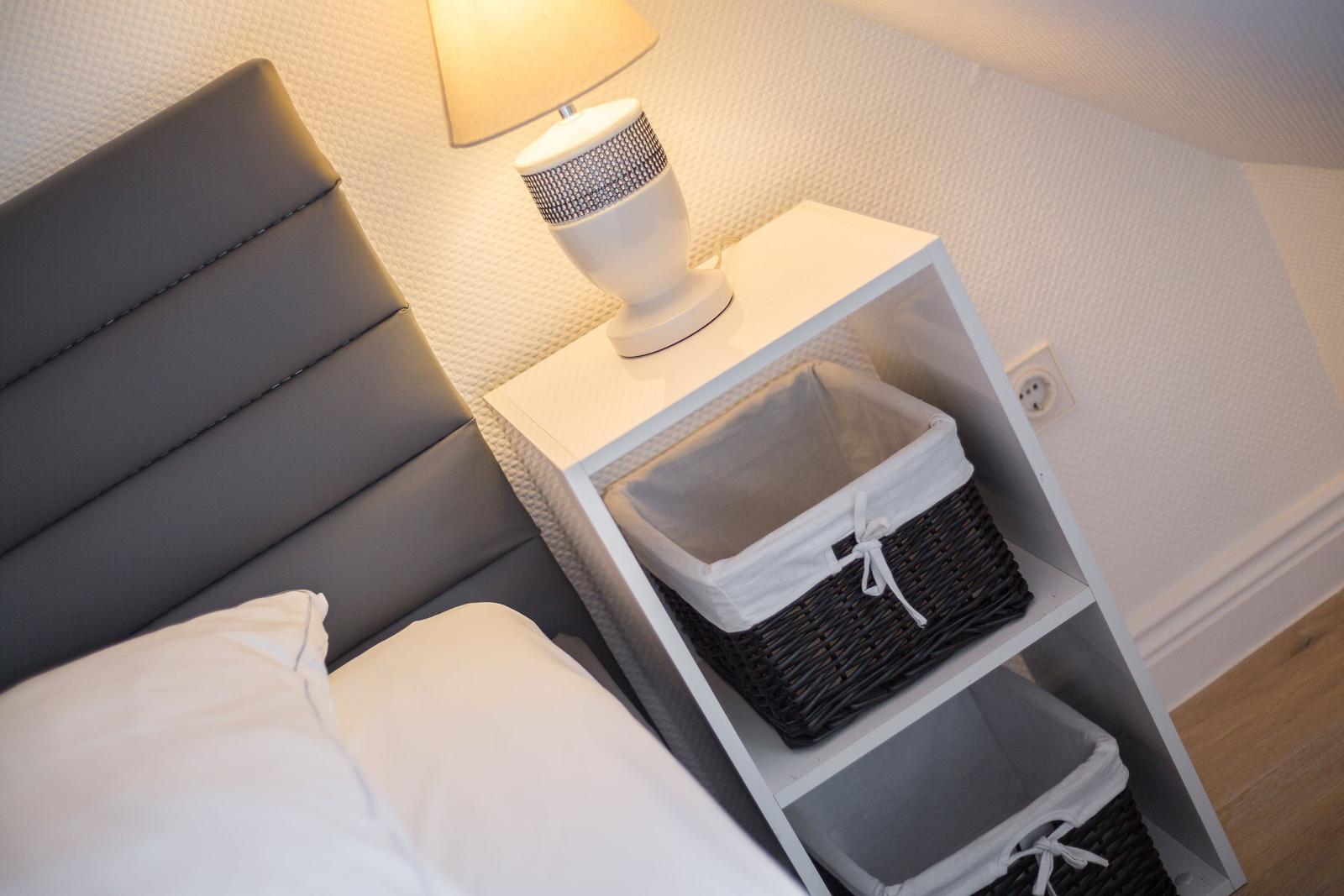 Schlafzimmer mit grauem Kopfteil, weißem Nachttisch und Lampe.