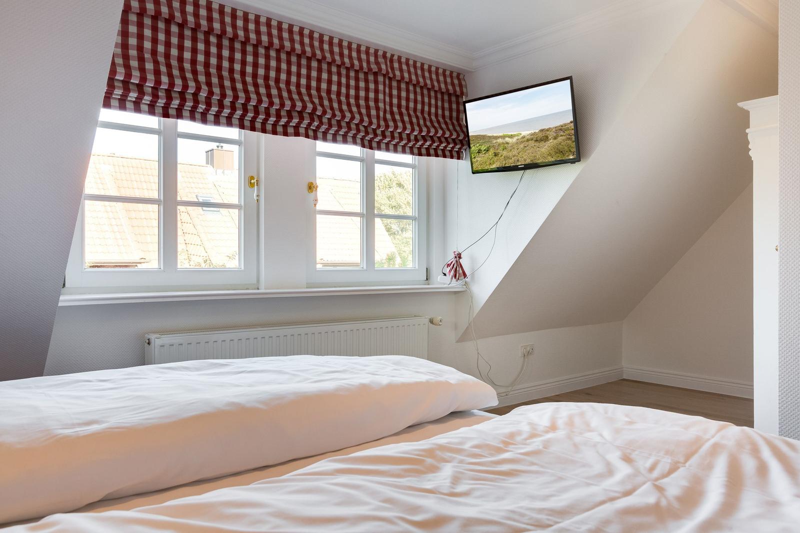 Schlafzimmer mit Dachschrägen, Fenster und TV. Bett mit weißer Bettwäsche.