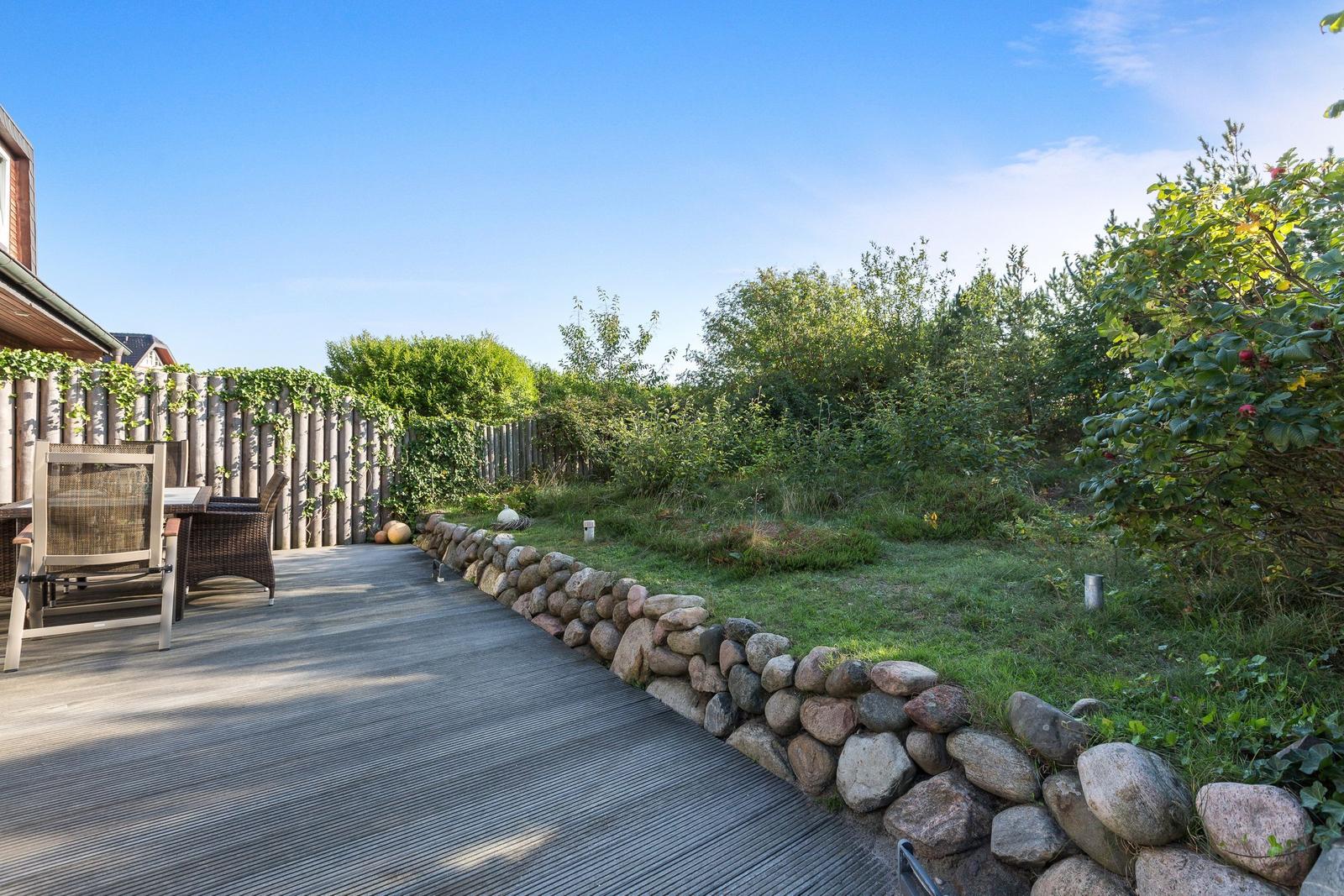 Holzterrasse mit Garten, Steinmauer und Sitzgelegenheiten.