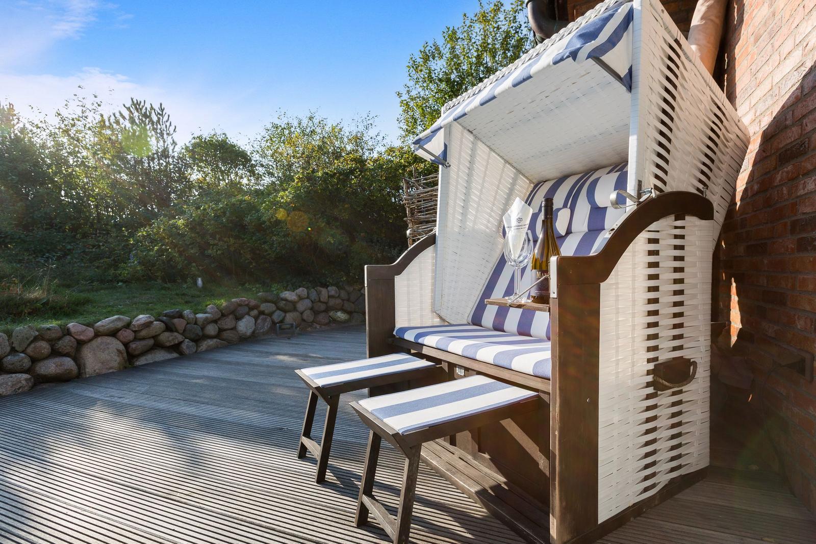 Hochwertiger Strandkorb mit blau-weißem Polster und Holzgestell auf Holzterrasse.