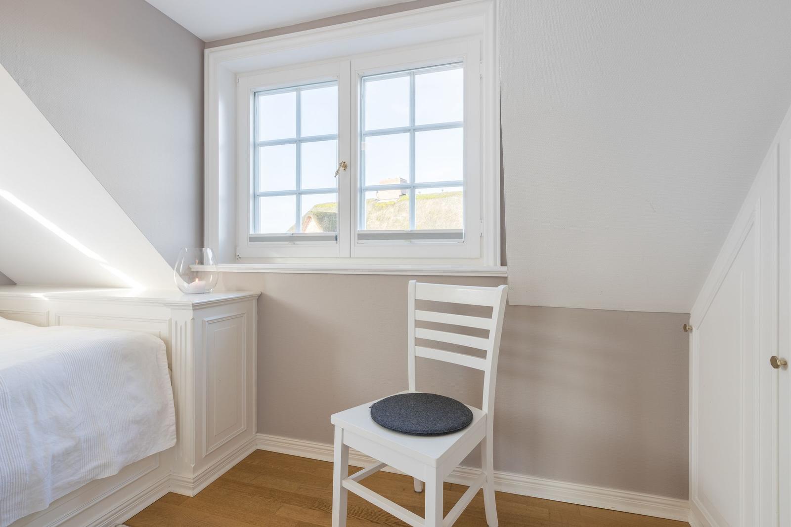 Bedroom with white bed, chair, and window. Wooden floor and two-tone walls.