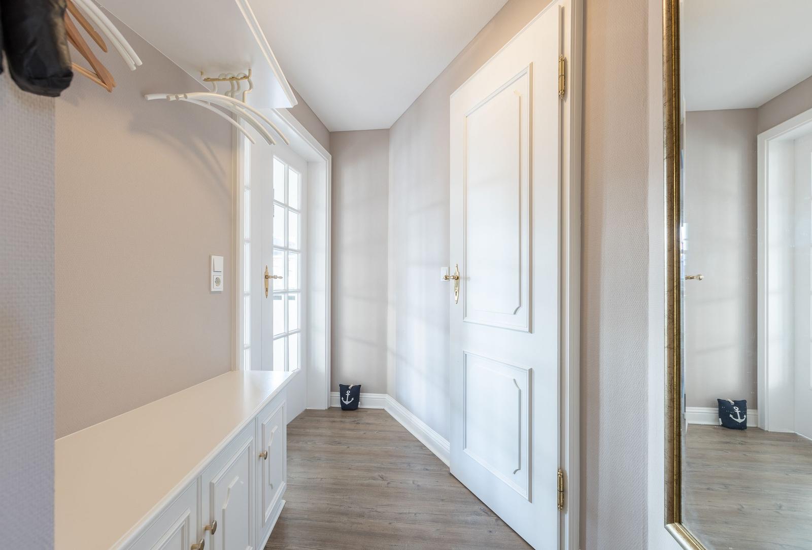 Hallway with coat rack, door, and mirror. Wooden floor and white doors.