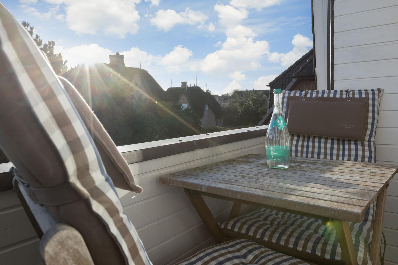 Terrace with table, chairs, and water bottle. View of rooftops and hills under blue sky.