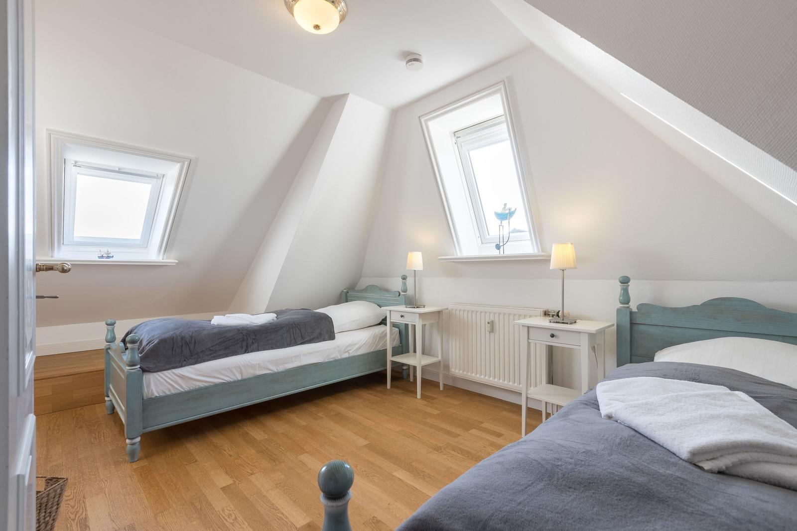 Two bedrooms with sloped ceilings, wooden floors, and windows.