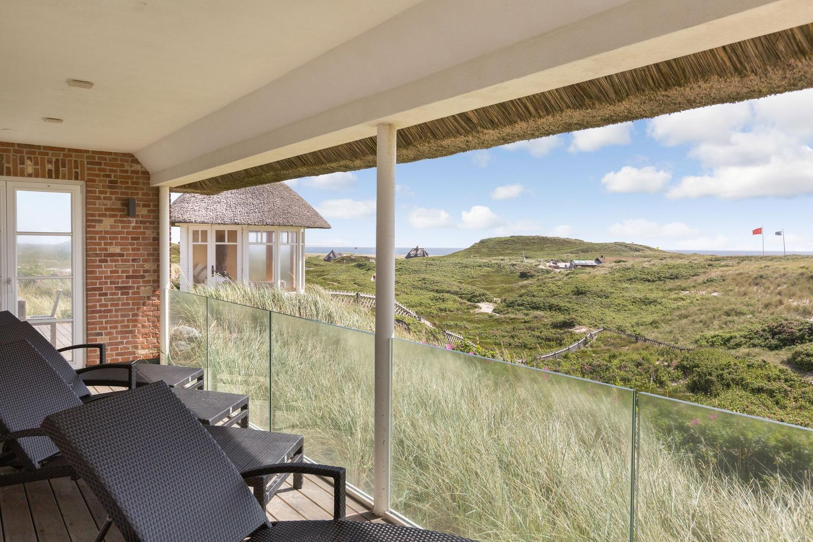 Terrasse mit Liegen und Blick auf Dünen und Strand.