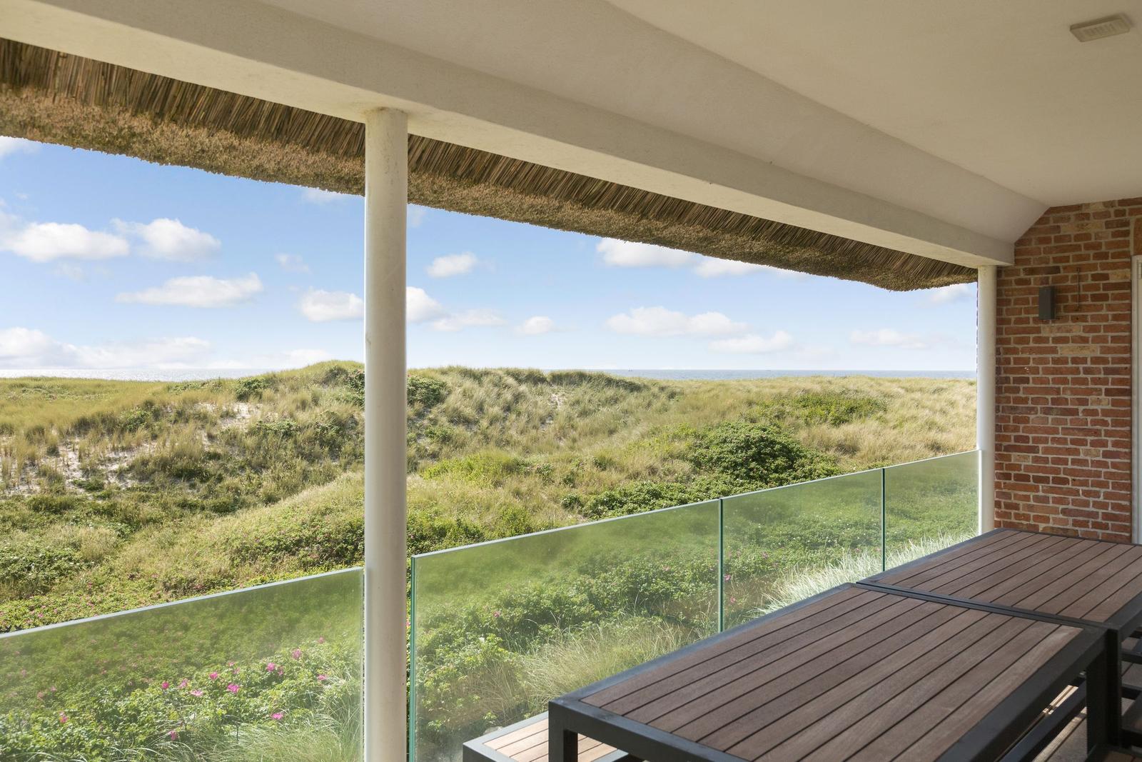 Terrasse mit Blick auf Dünen und Meer unter strohgedecktem Dach.