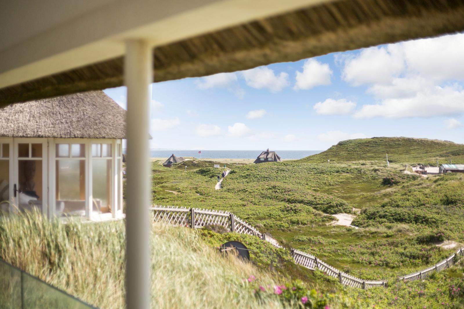 Von der Veranda aus blickt man auf grüne Dünen, einen See und traditionelle Häuser mit Strohdächern.