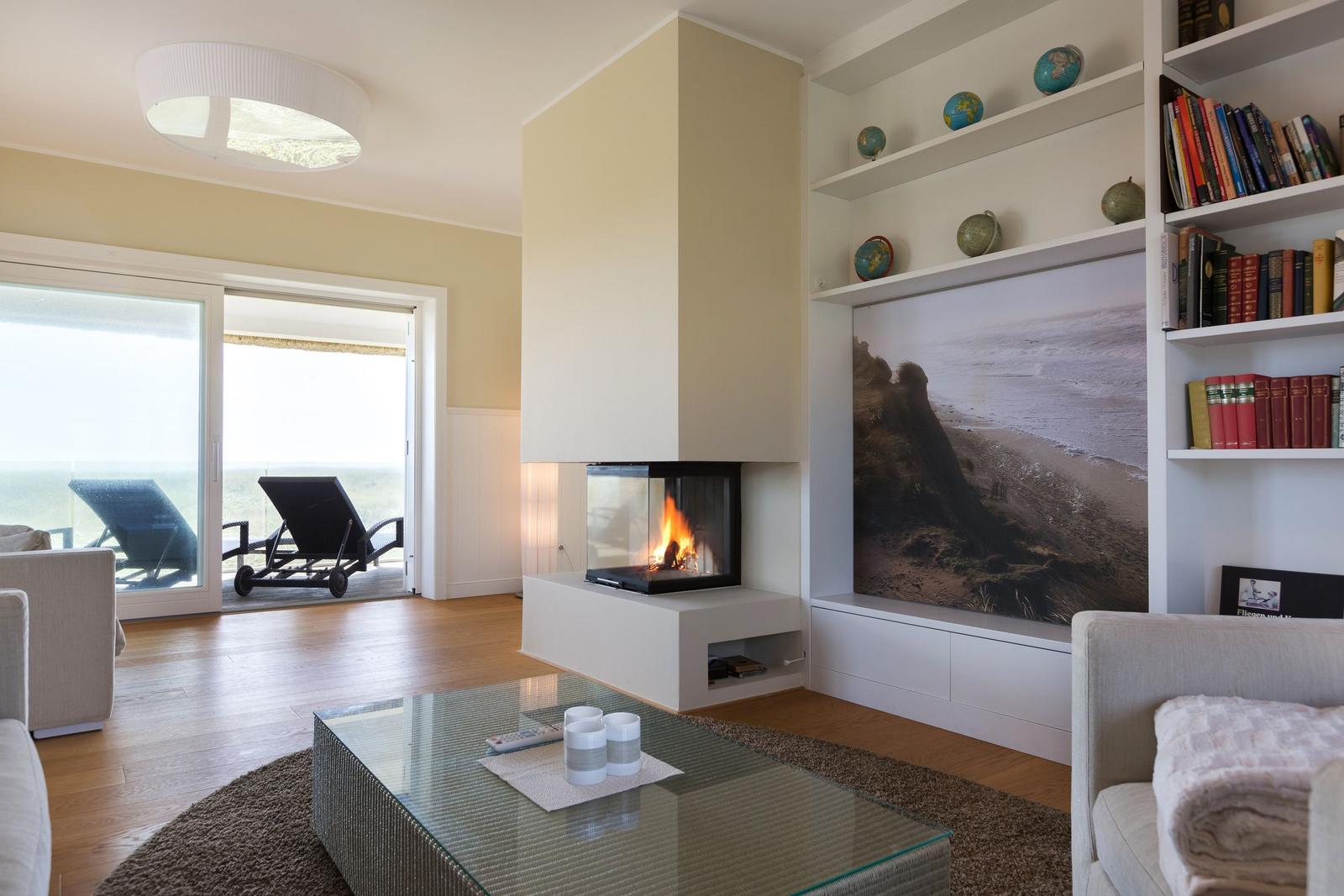 Wohnzimmer mit Kamin, Bücherregal und Terrasse mit Liegestühlen.