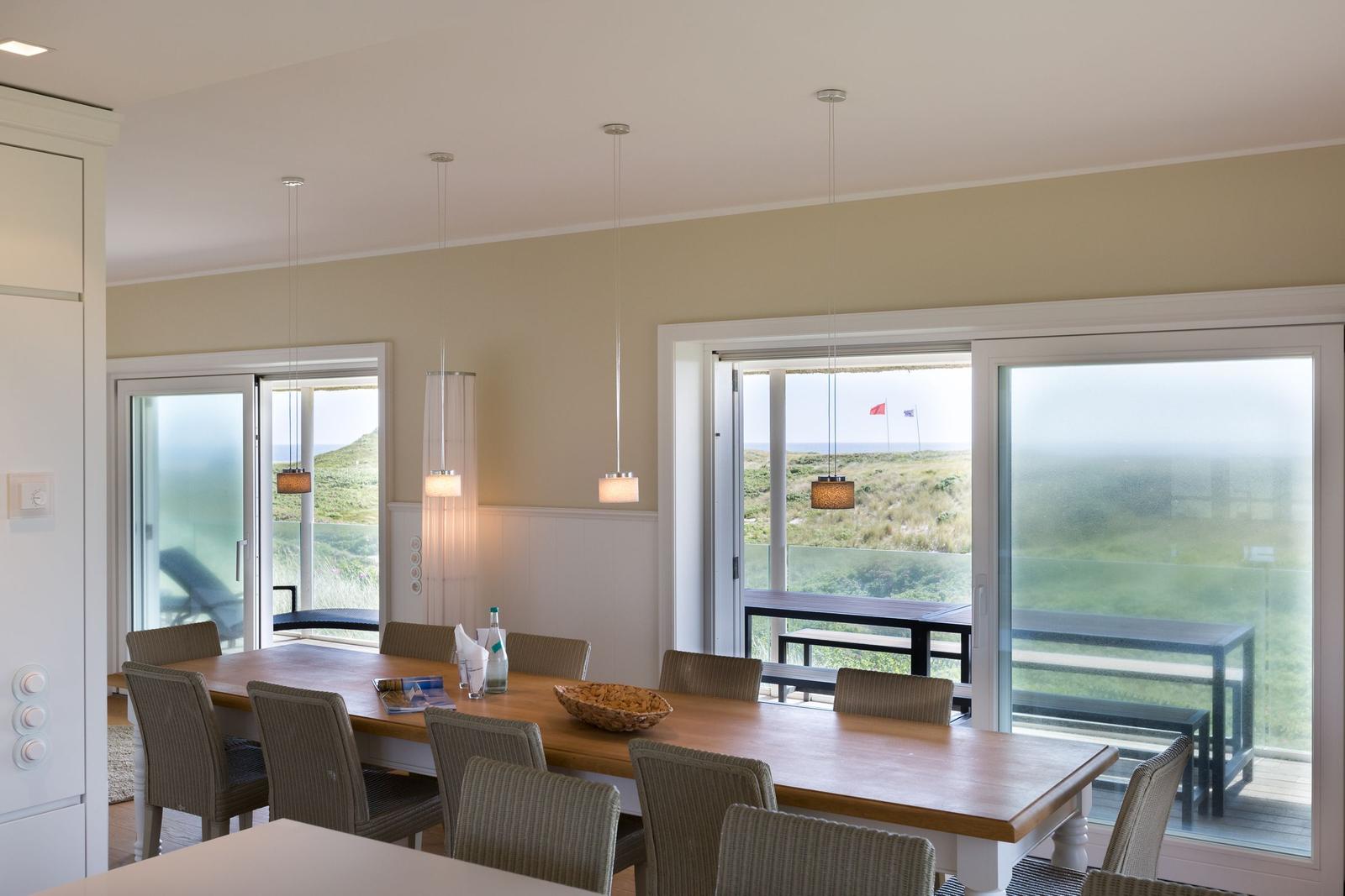 Esszimmer mit Tisch, Stühlen und Blick auf Grasland und Meer.