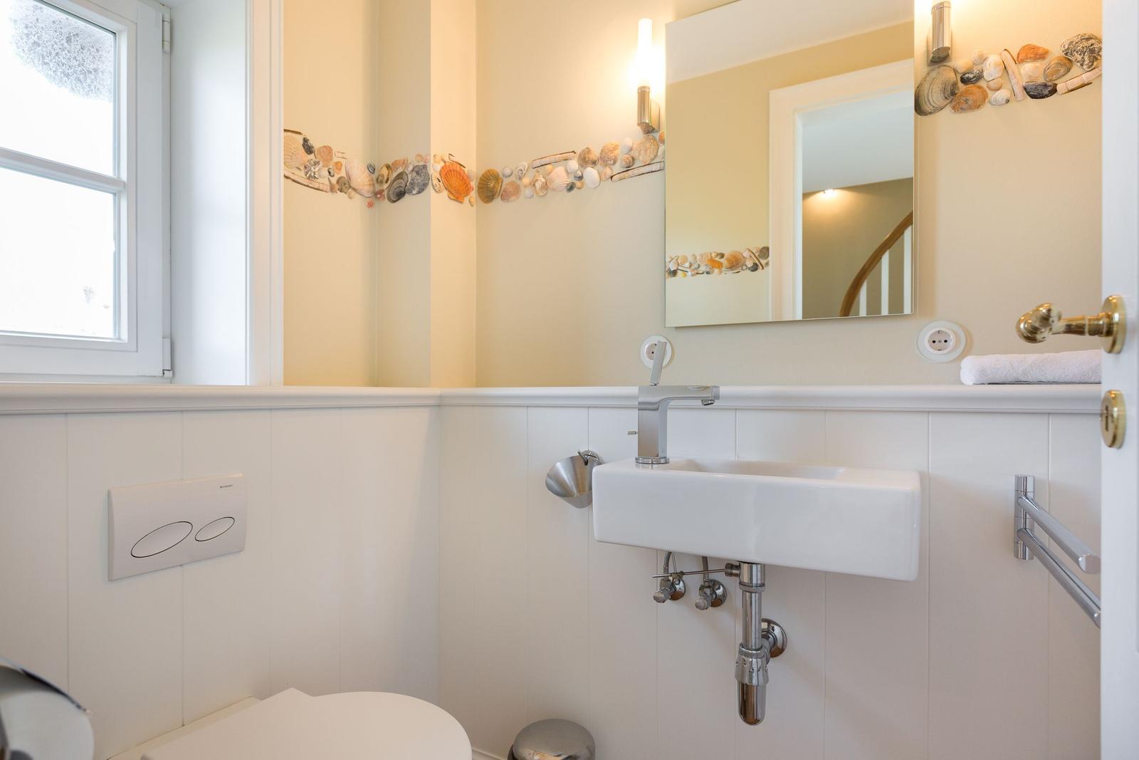 Badezimmer mit Waschbecken, Spiegel und Fenster. Wandverkleidung und Muscheldekor.