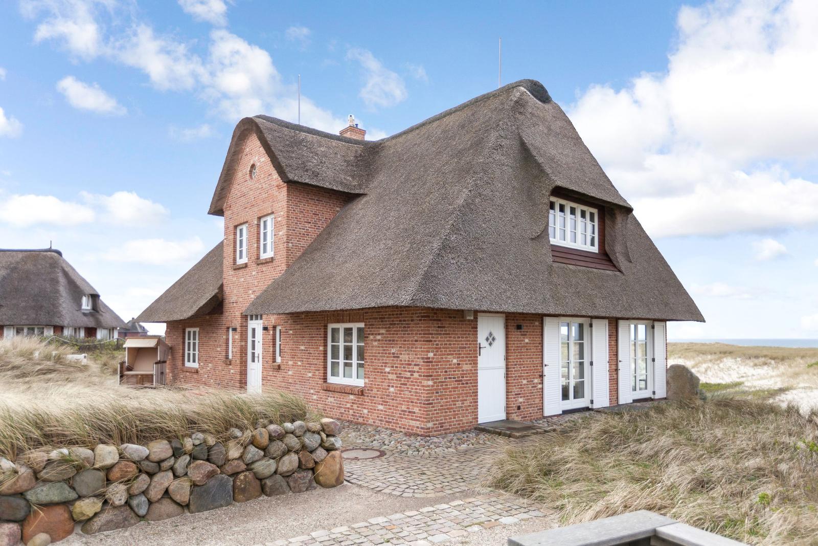 Rotes Backsteinhaus mit strohgedecktem Dach und weißen Fenstern an Strand