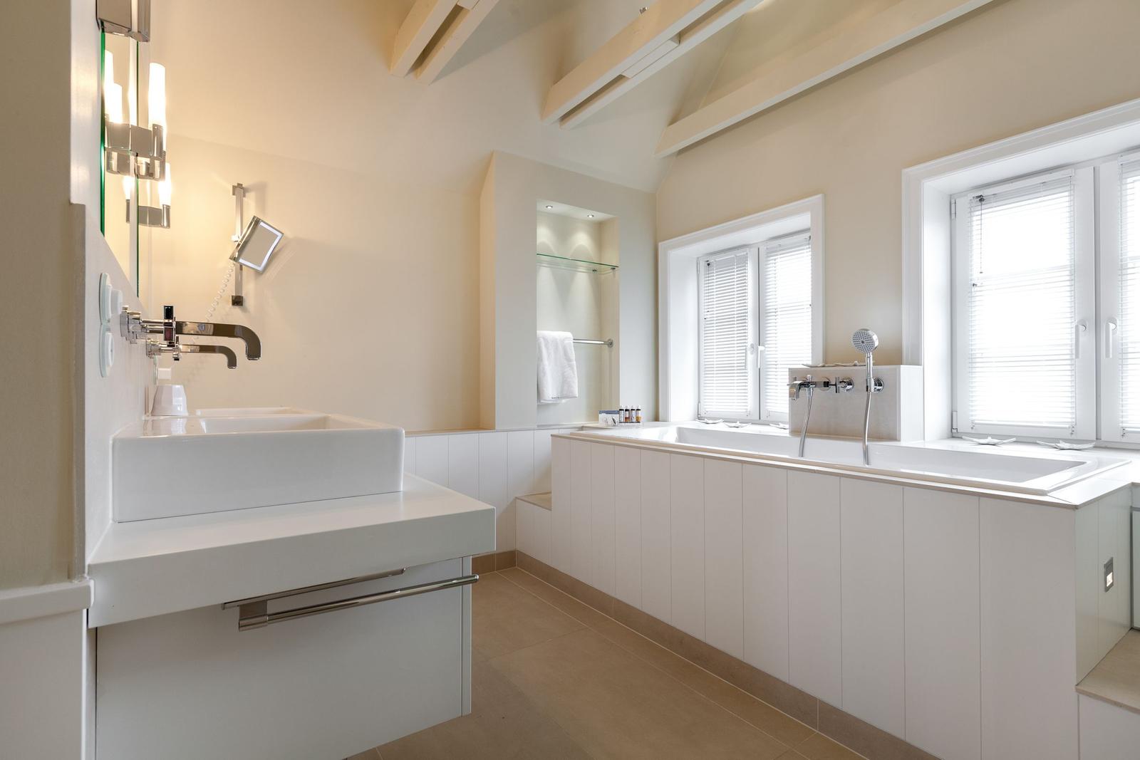 Badezimmer mit Badewanne, Waschbecken und Fenstern.