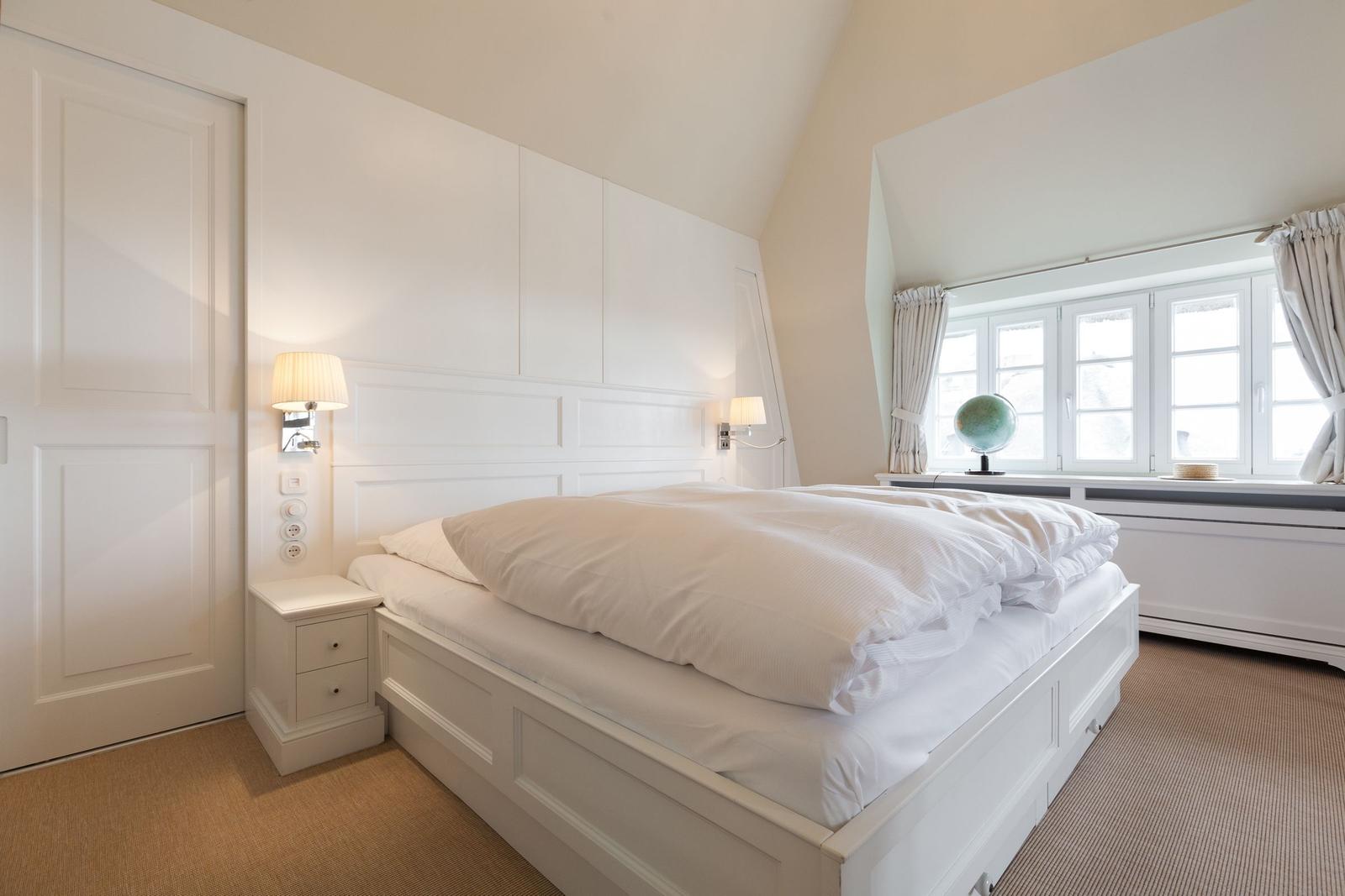 Schlafzimmer mit weißem Bett, Nachttisch und Fenster