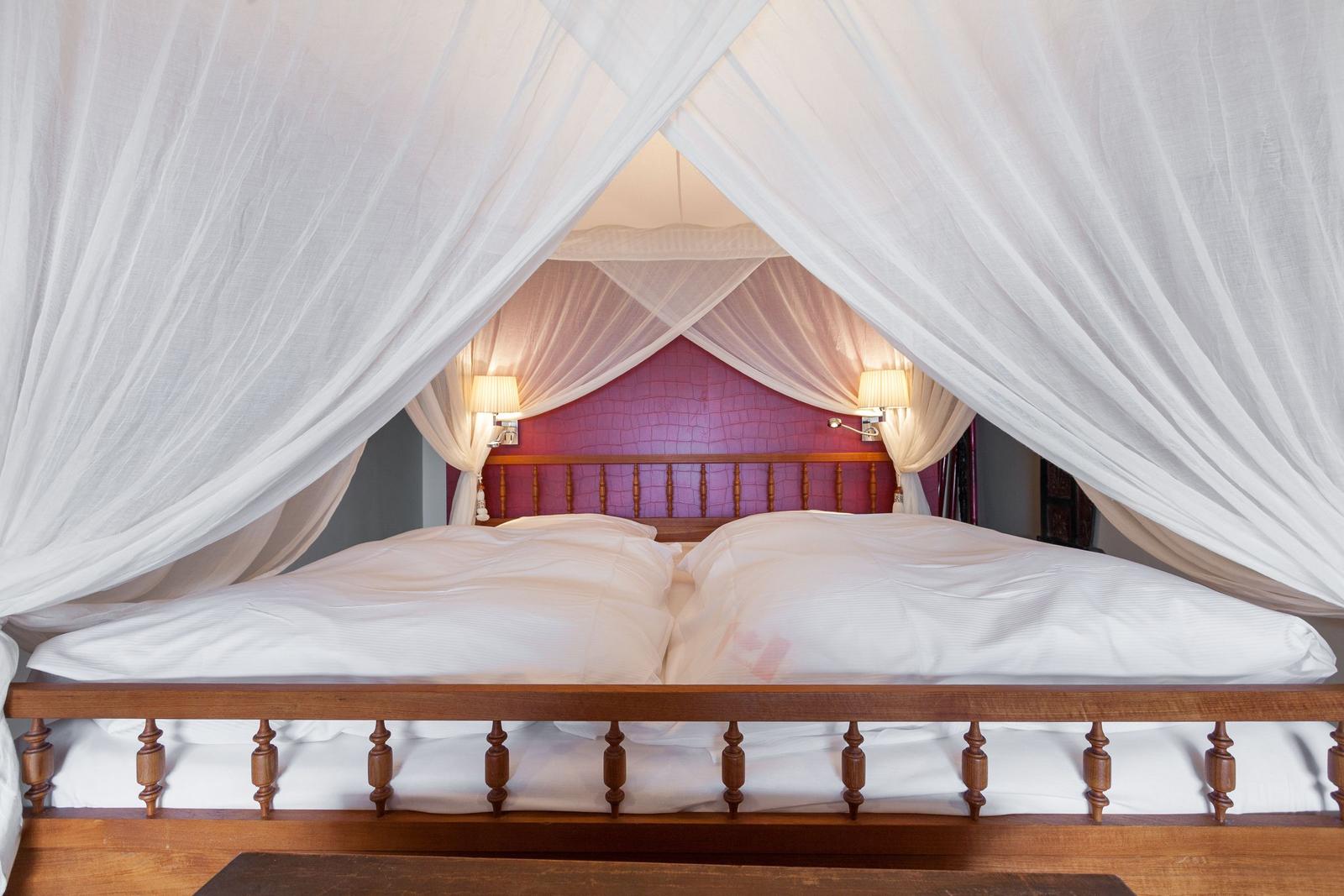 Hochbetten mit weißer Bettwäsche und weißen Vorhängen. Hinter dem Bett steht eine rosa Wand.