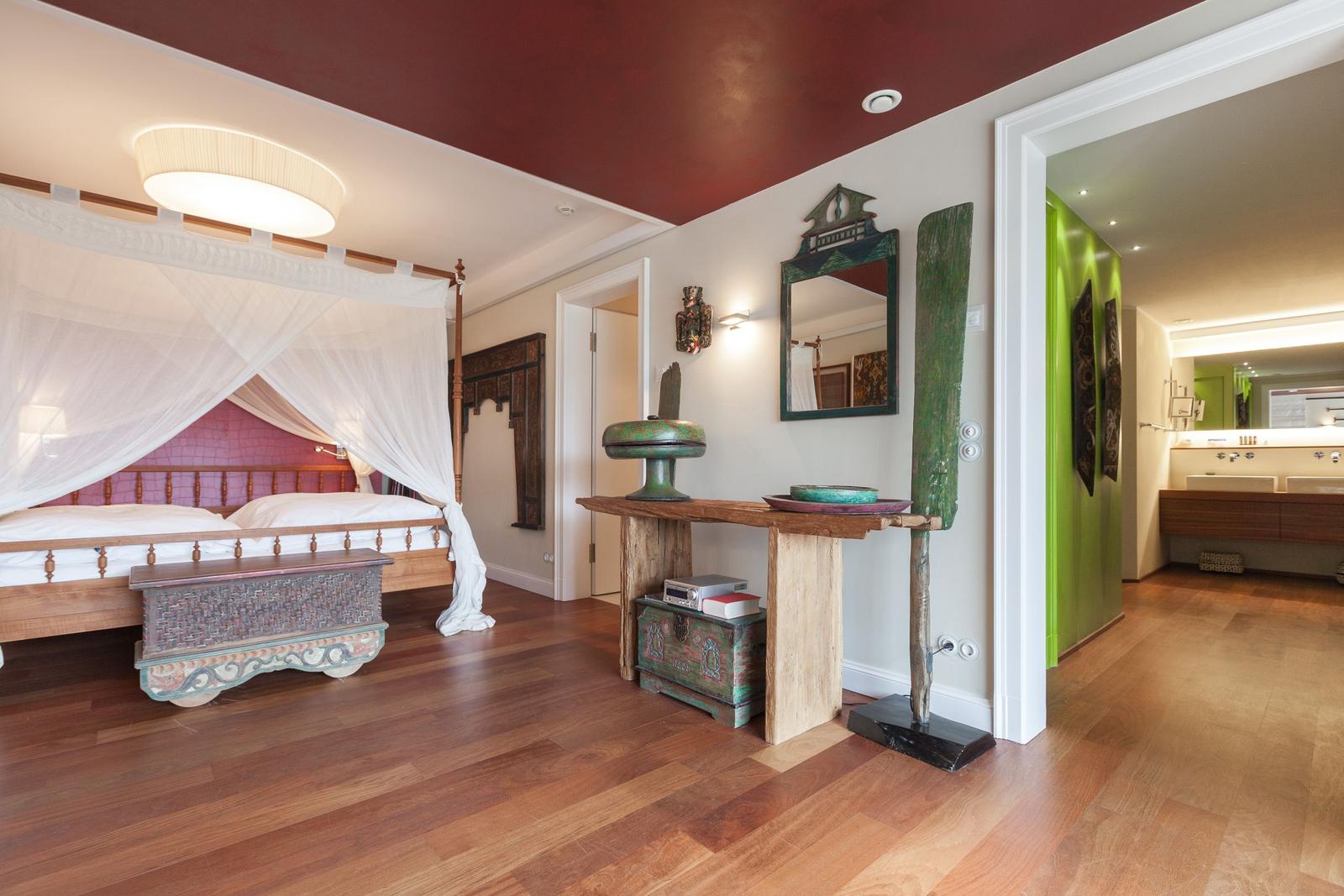Schlafzimmer mit Himmelbett, Holzboden und dekorativen Möbeln. Badezimmer mit grüner Wand sichtbar.