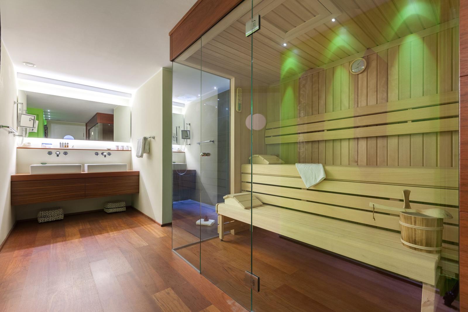 Sauna mit Holzbänken und Glaswand. Neben dem Bad mit Dusche und Waschbecken.