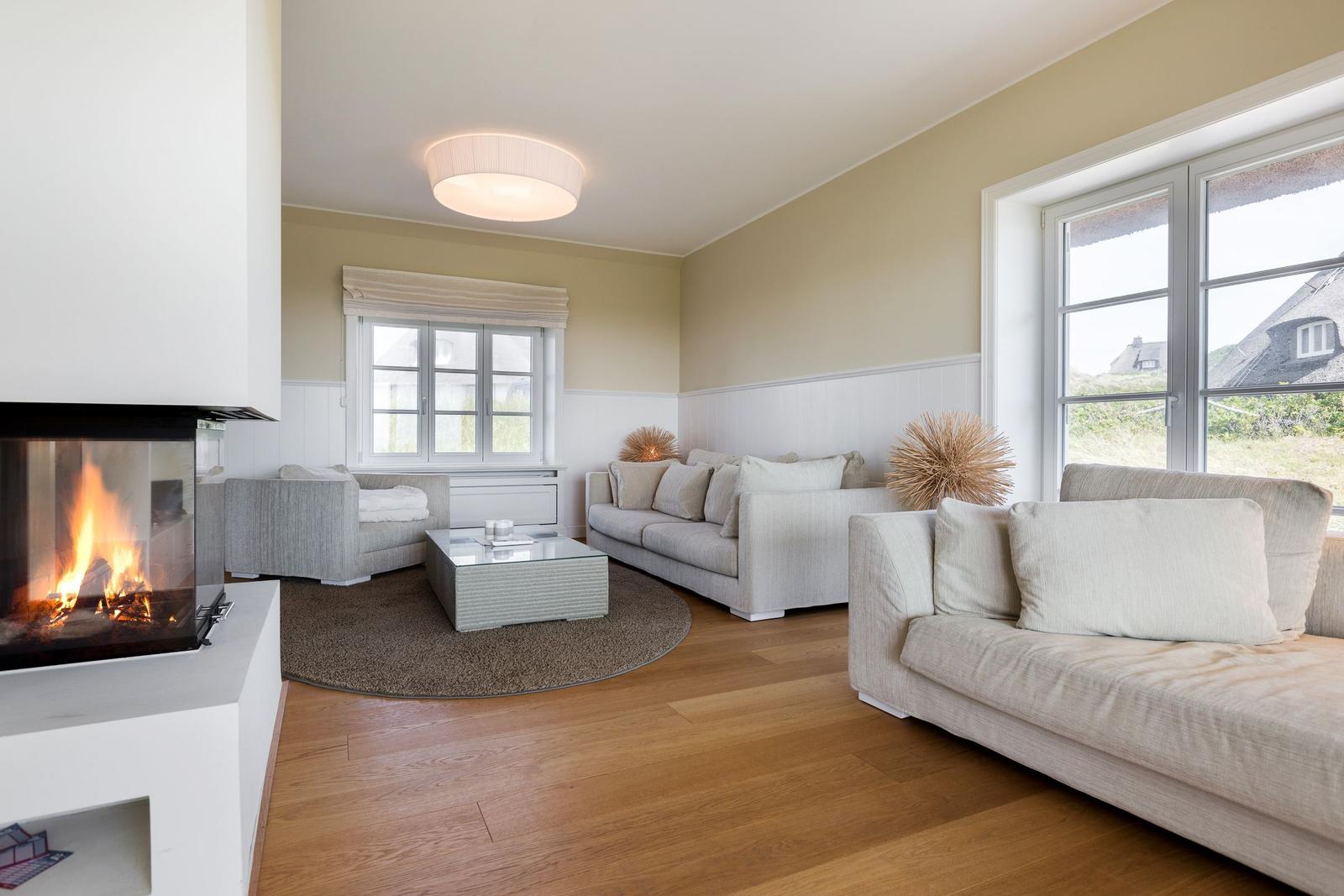 Wohnzimmer mit Kamin, Sofa und Holzboden. Fenster zeigen Landschaft.
