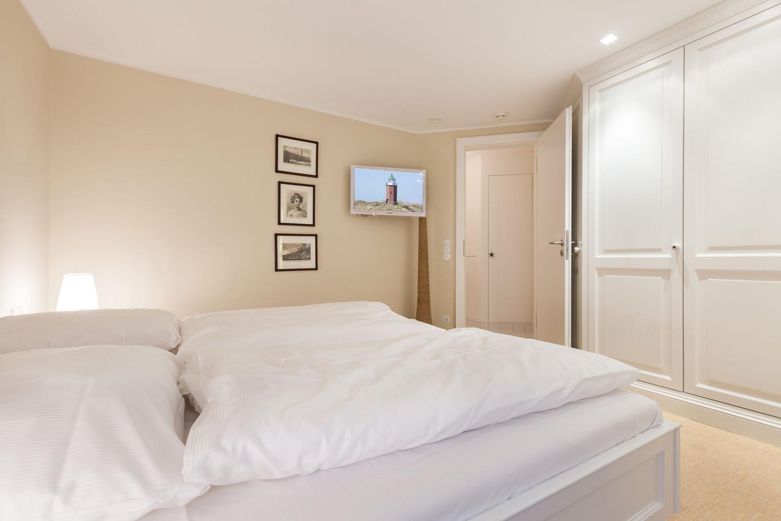 Schlafzimmer mit weißem Bett, Kleiderschrank und Wandbildern.