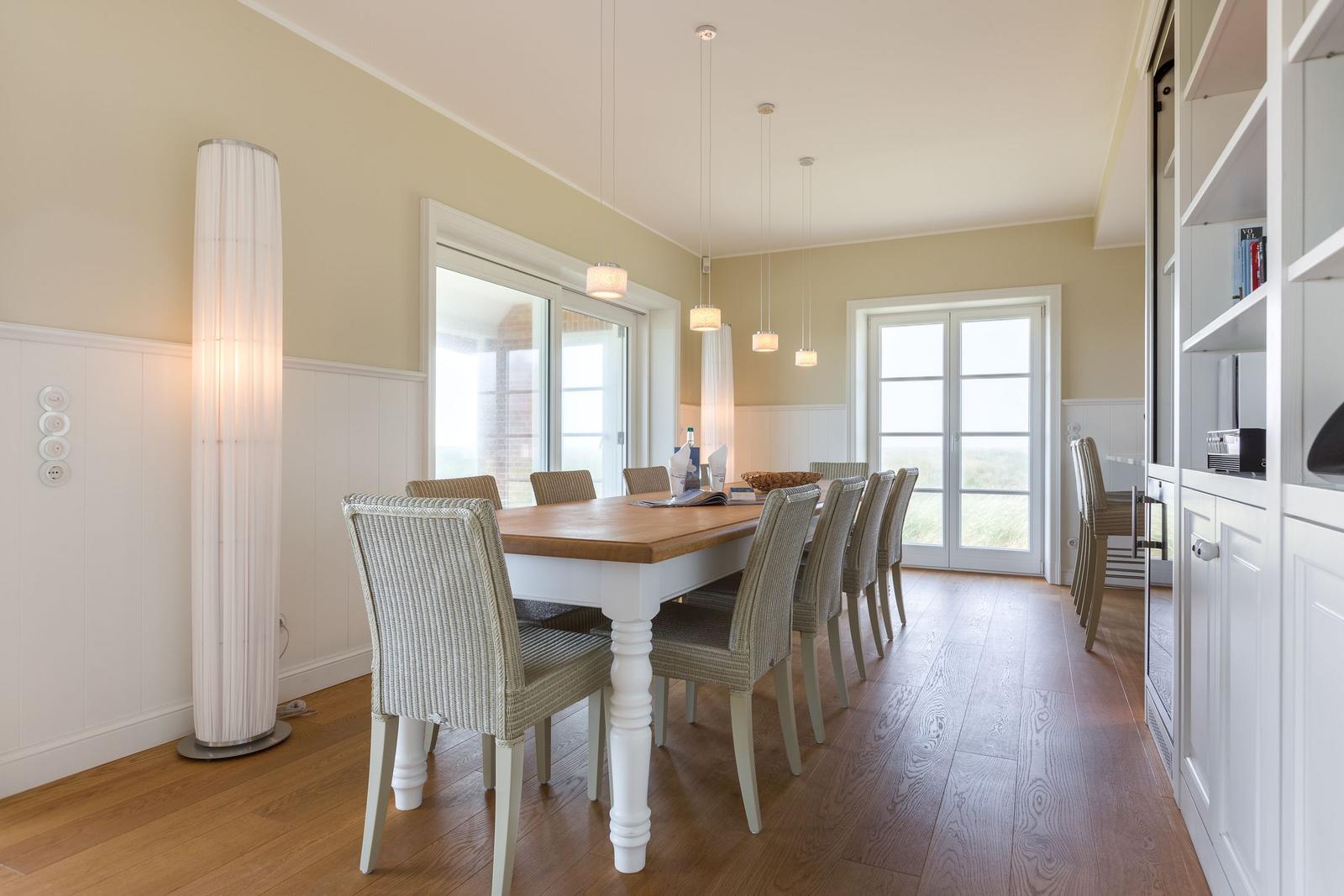 Esszimmer mit Holztisch, Stühlen und Fenstern. Weiße Einbaumöbel und Stehlampe.