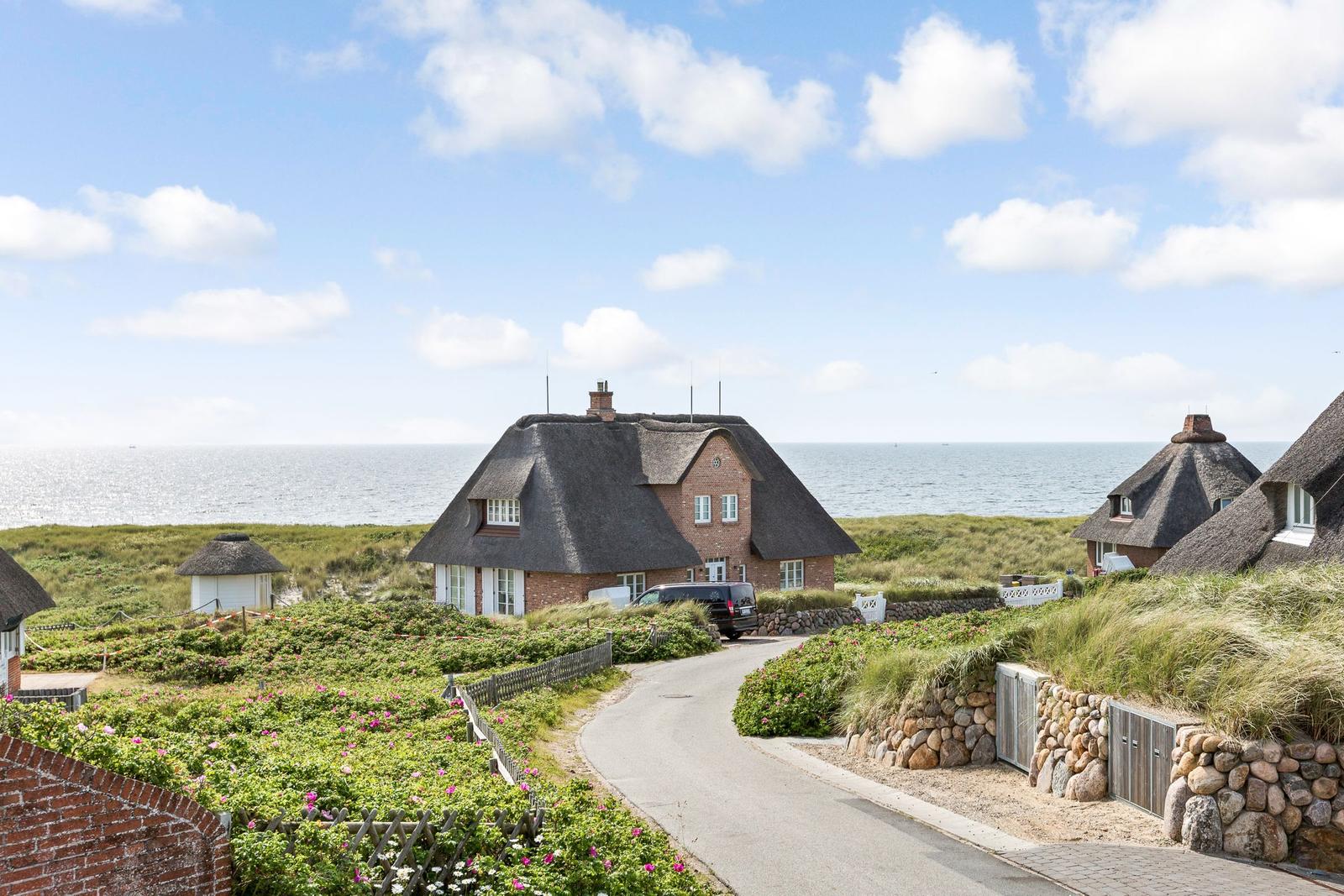 Haus mit Strohdach am Meer, gepflasterter Weg und Blumenbeete.