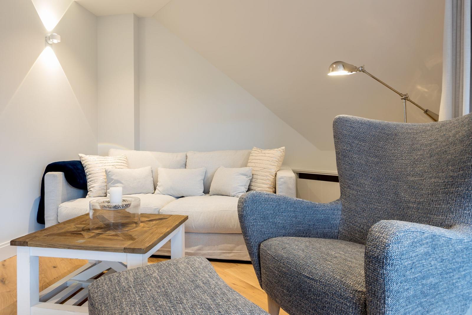 Wohnzimmer mit Sofa, Sessel und Tisch unter schrägen Wänden.