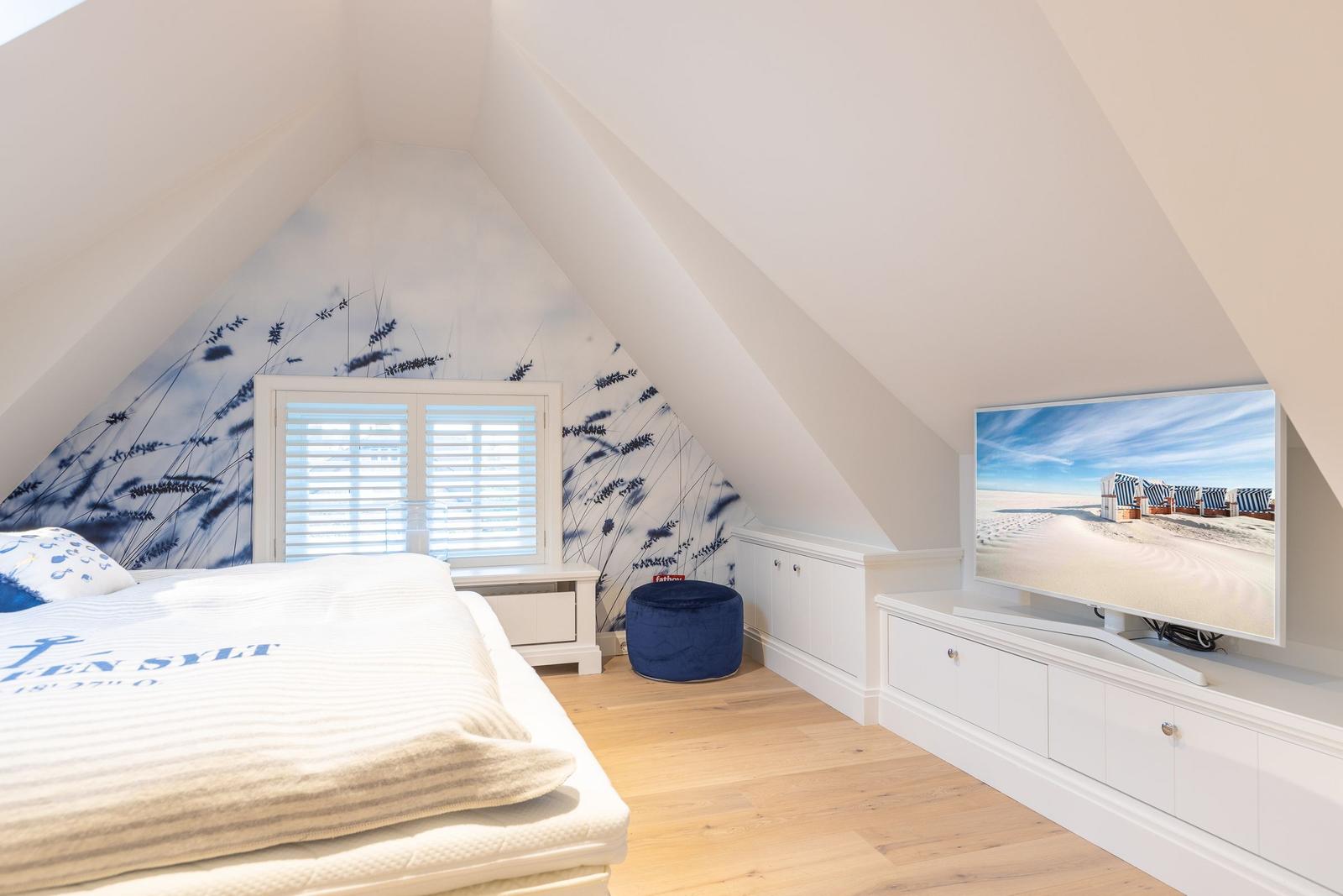 Schlafzimmer mit Dachschrägen, Bett, TV und Fenster mit Jalousie.