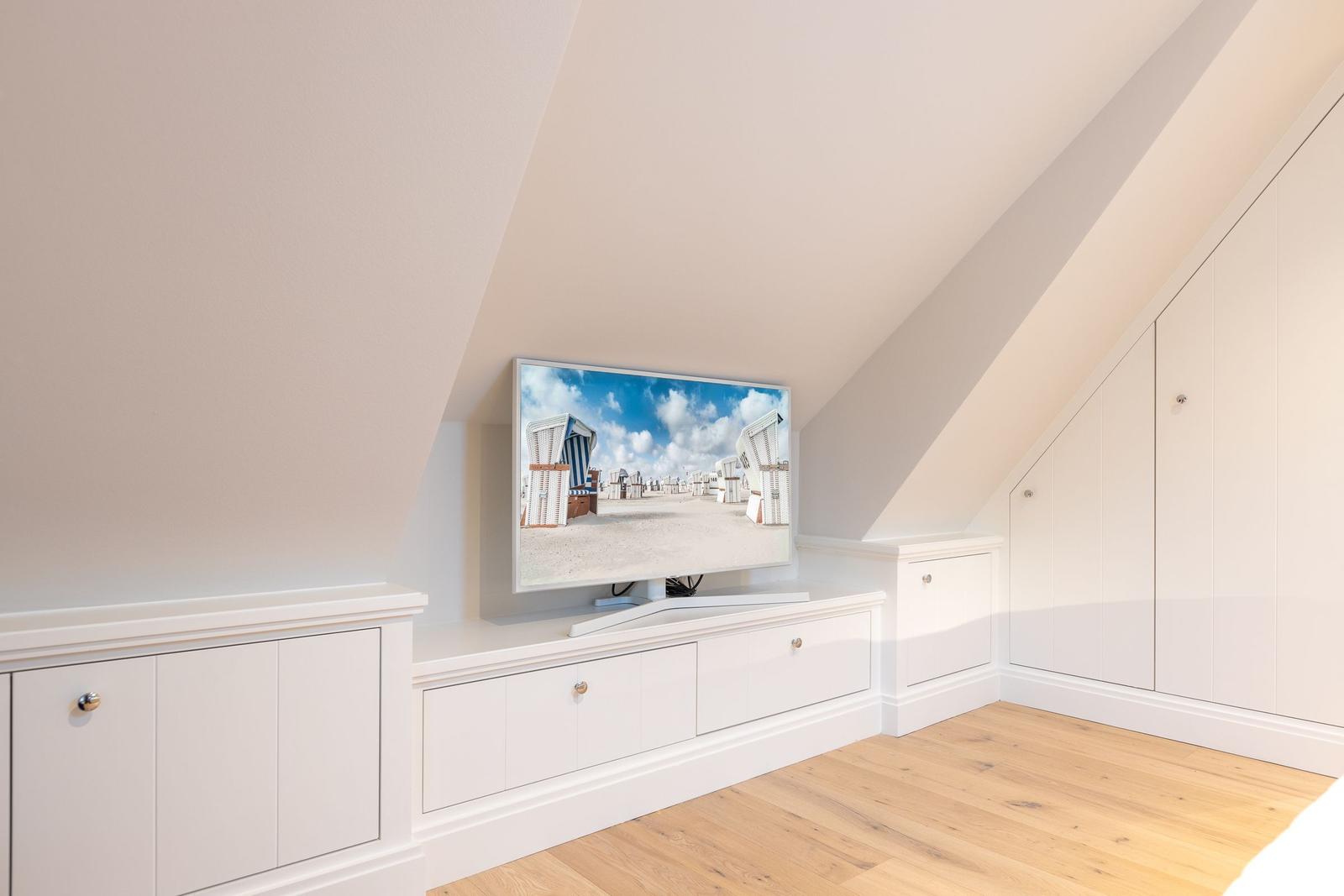 Dachgeschosszimmer mit TV und weißen Schränken.