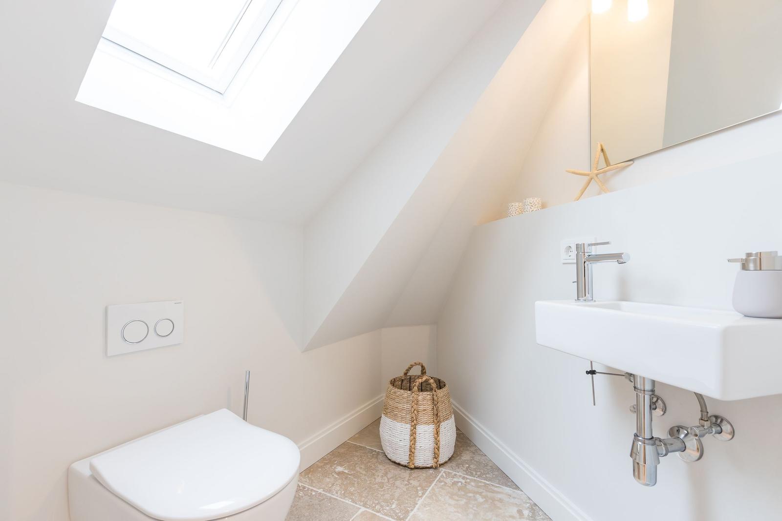 Duschbad mit Dachfenster, Waschbecken und Toilette. Holzkorb und Seestern dekorieren den Raum.