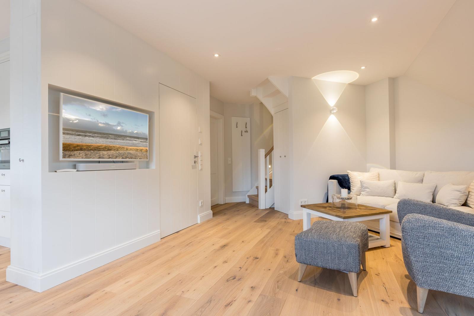 Wohnzimmer mit Sofa, Sitzhocker und Fernseher in Wandnische.