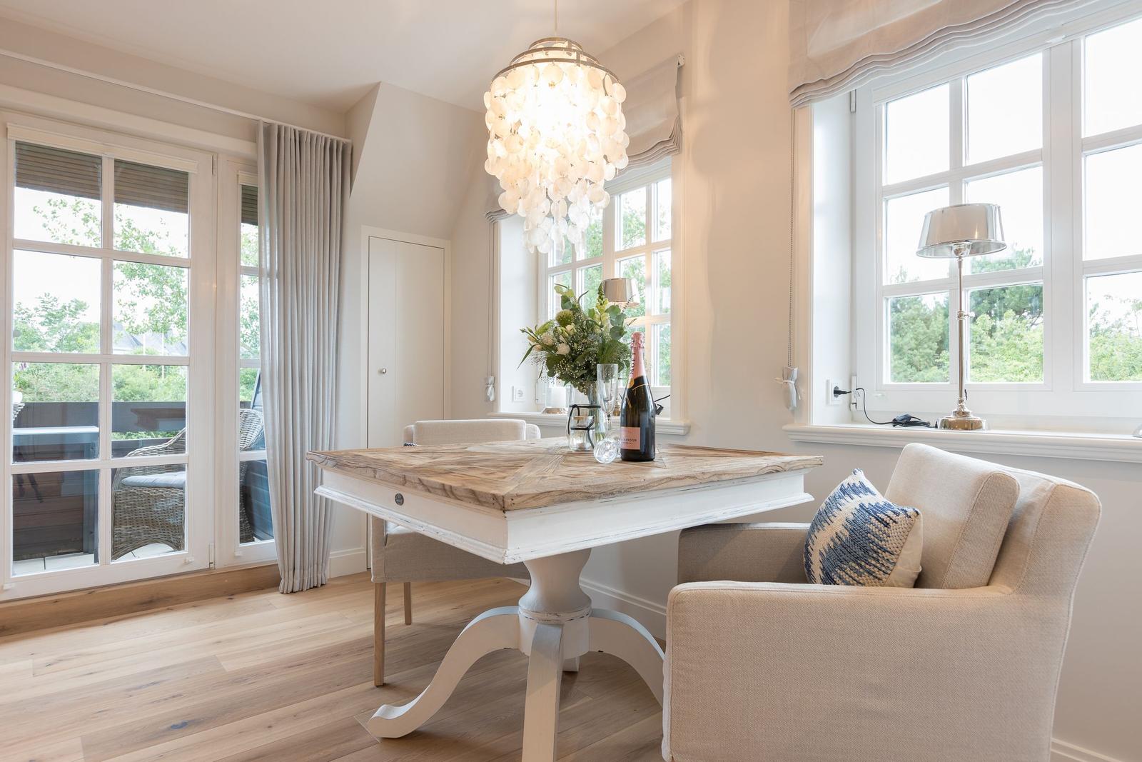 Esszimmer mit Holztisch, Stühlen und Fenstern. Deckenleuchte und Blumen auf Tisch.